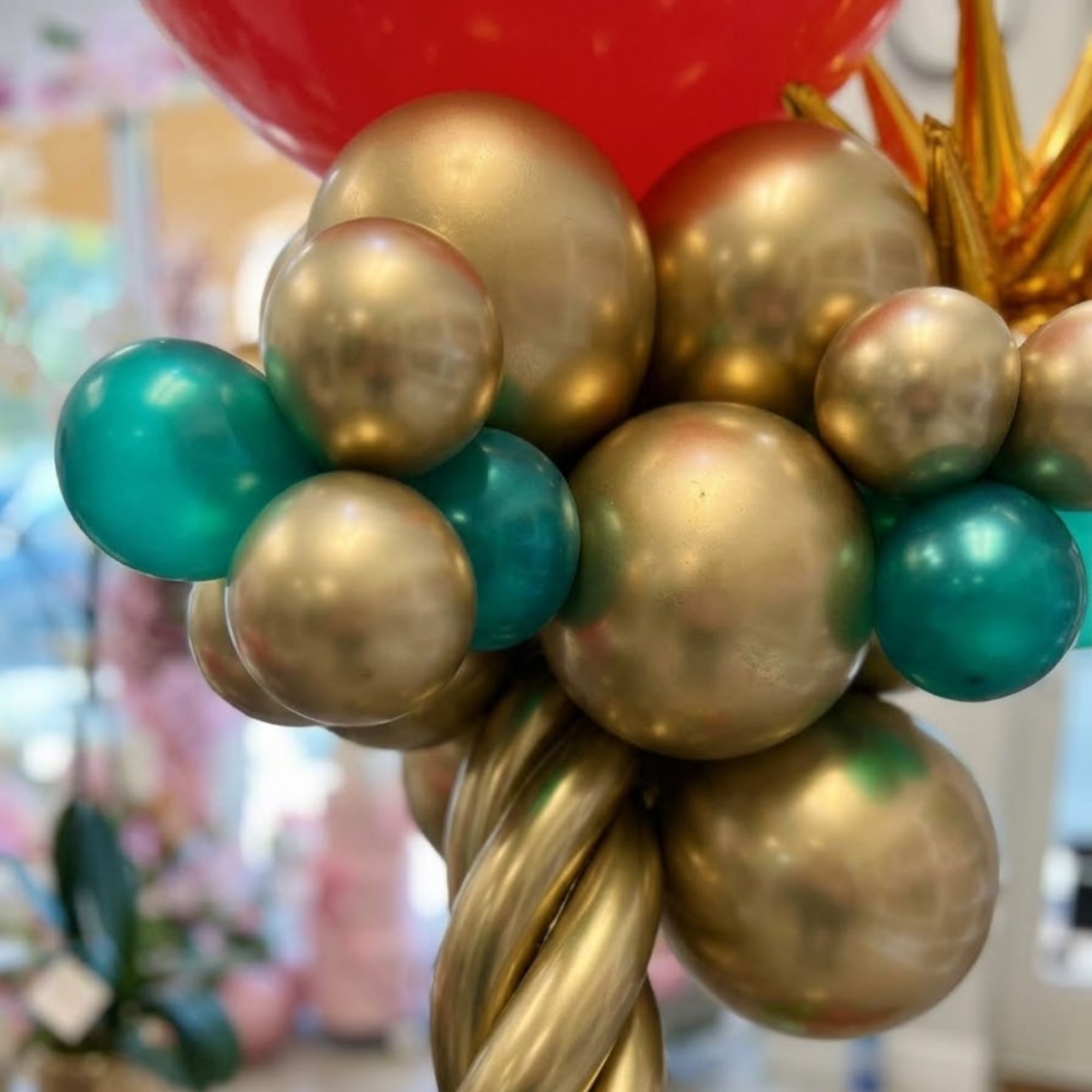 Cluster of gold, teal, and red balloons with a twisted gold balloon base