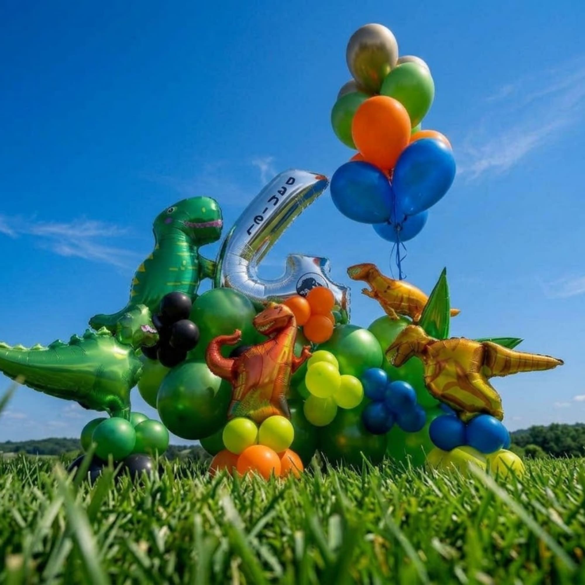 Cluster of dinosaur balloons and number balloons on grass under a blue sky