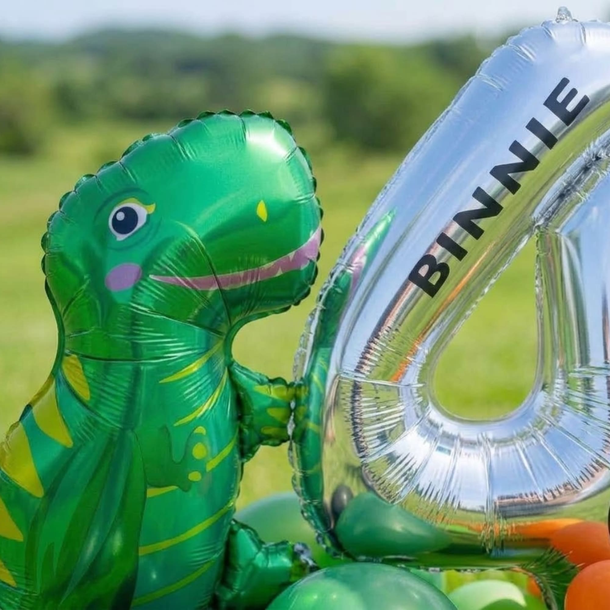Green dinosaur balloon beside a silver number balloon outdoors