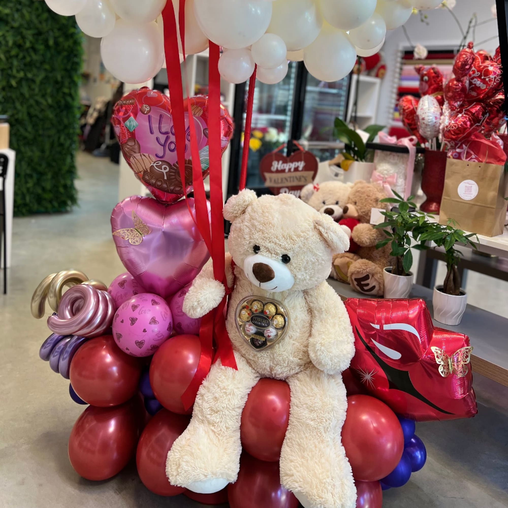 Teddy bear sitting on a balloon arrangement with heart balloons and chocolates