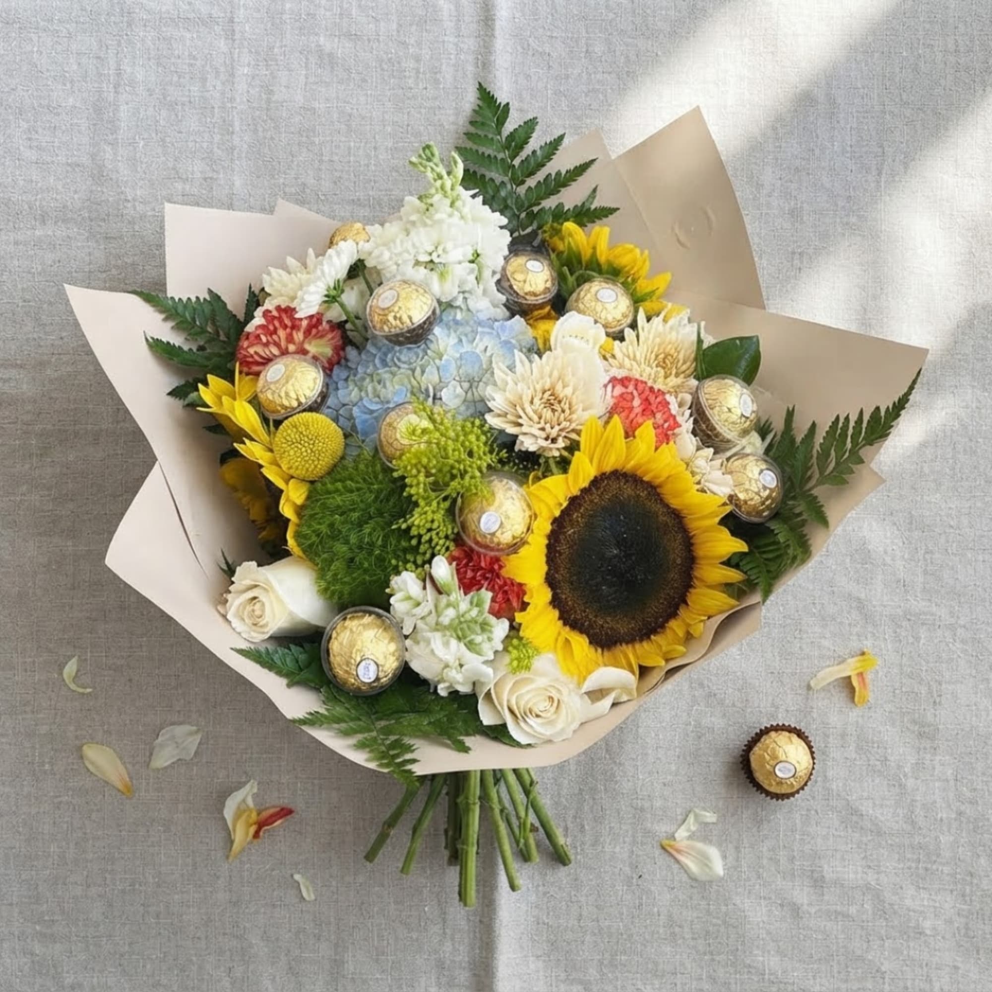 Bouquet of sunflowers, roses, and mixed blooms with chocolates wrapped in paper