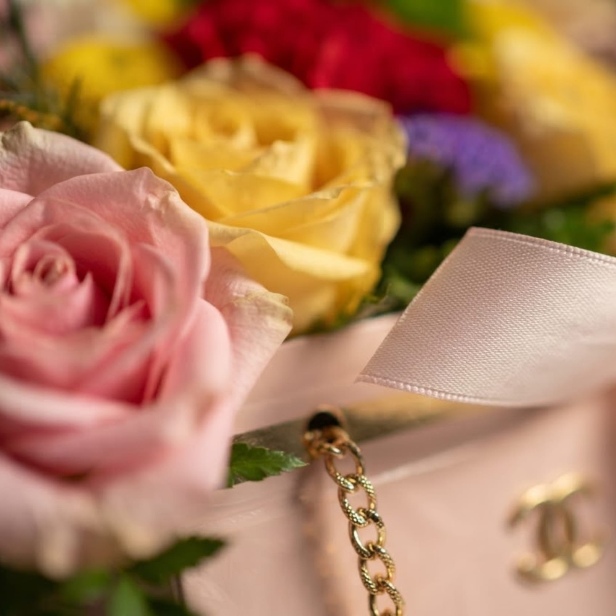 Close-up of pink and yellow roses with a satin ribbon and gold chain detail