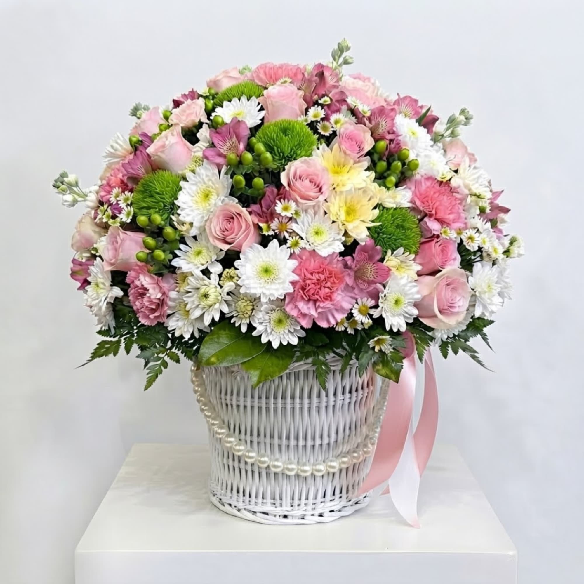 Pink and white mixed flower arrangement in a white wicker basket with ribbon