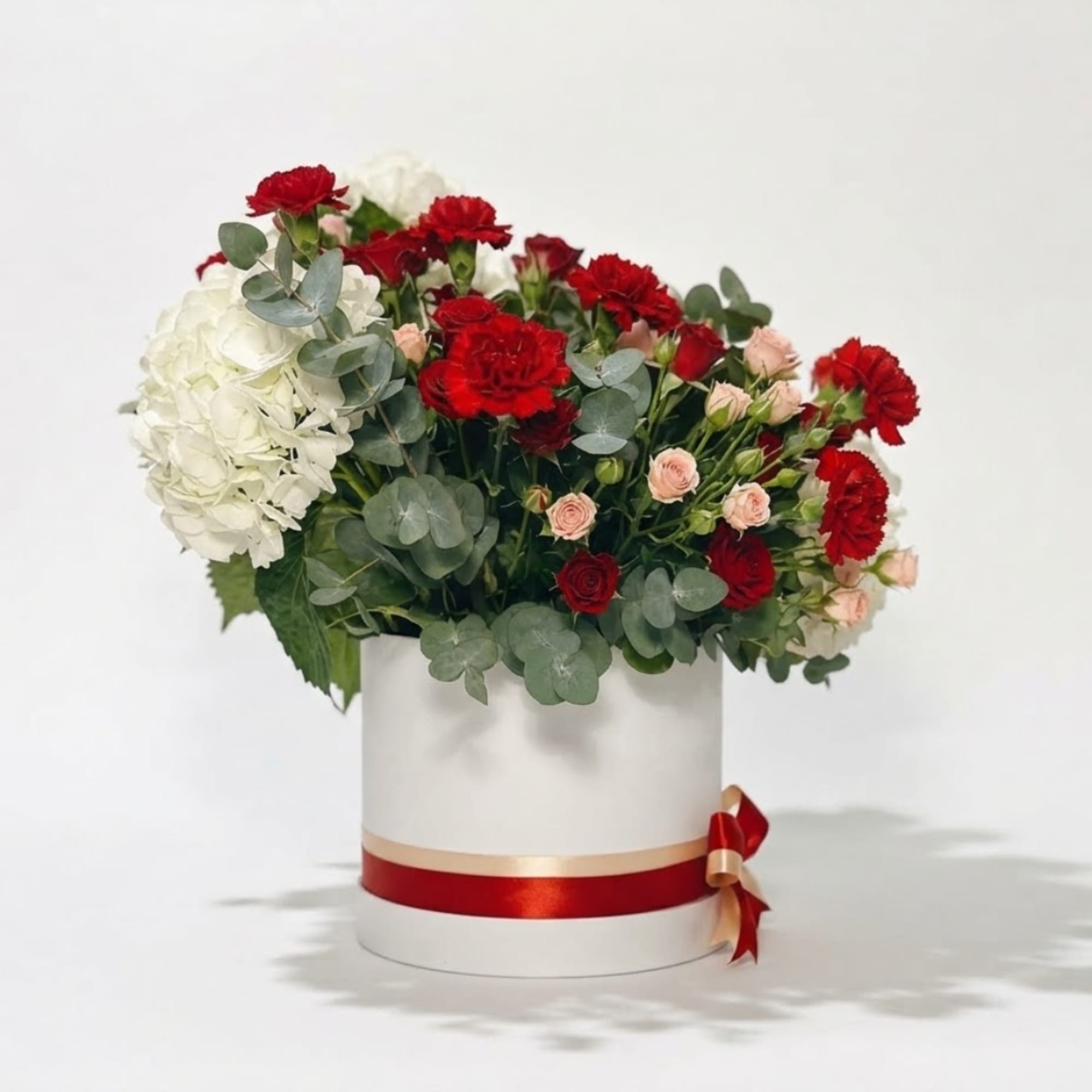 Red and white floral arrangement in a white round box with a ribbon