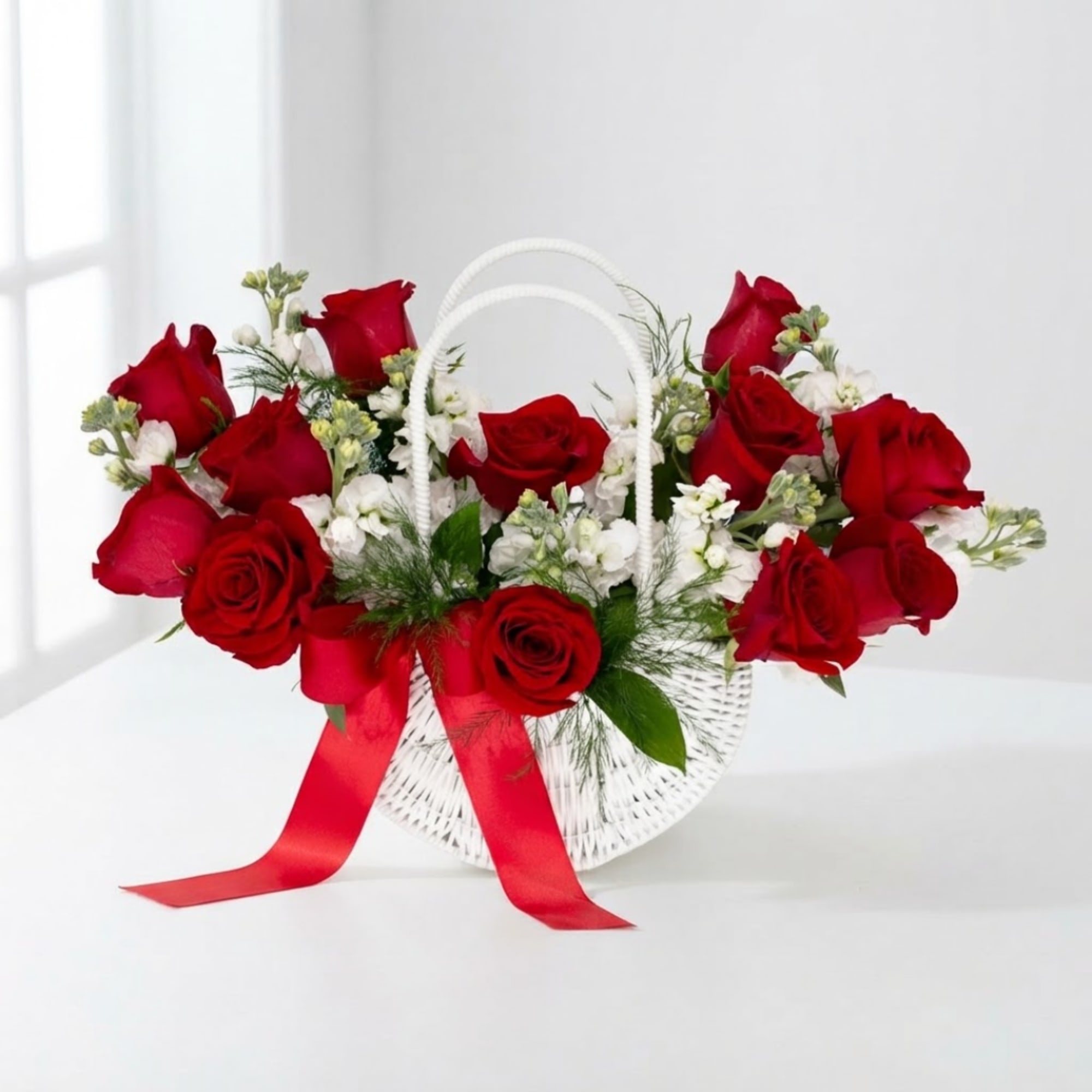 Red roses arranged in a white basket with a red ribbon