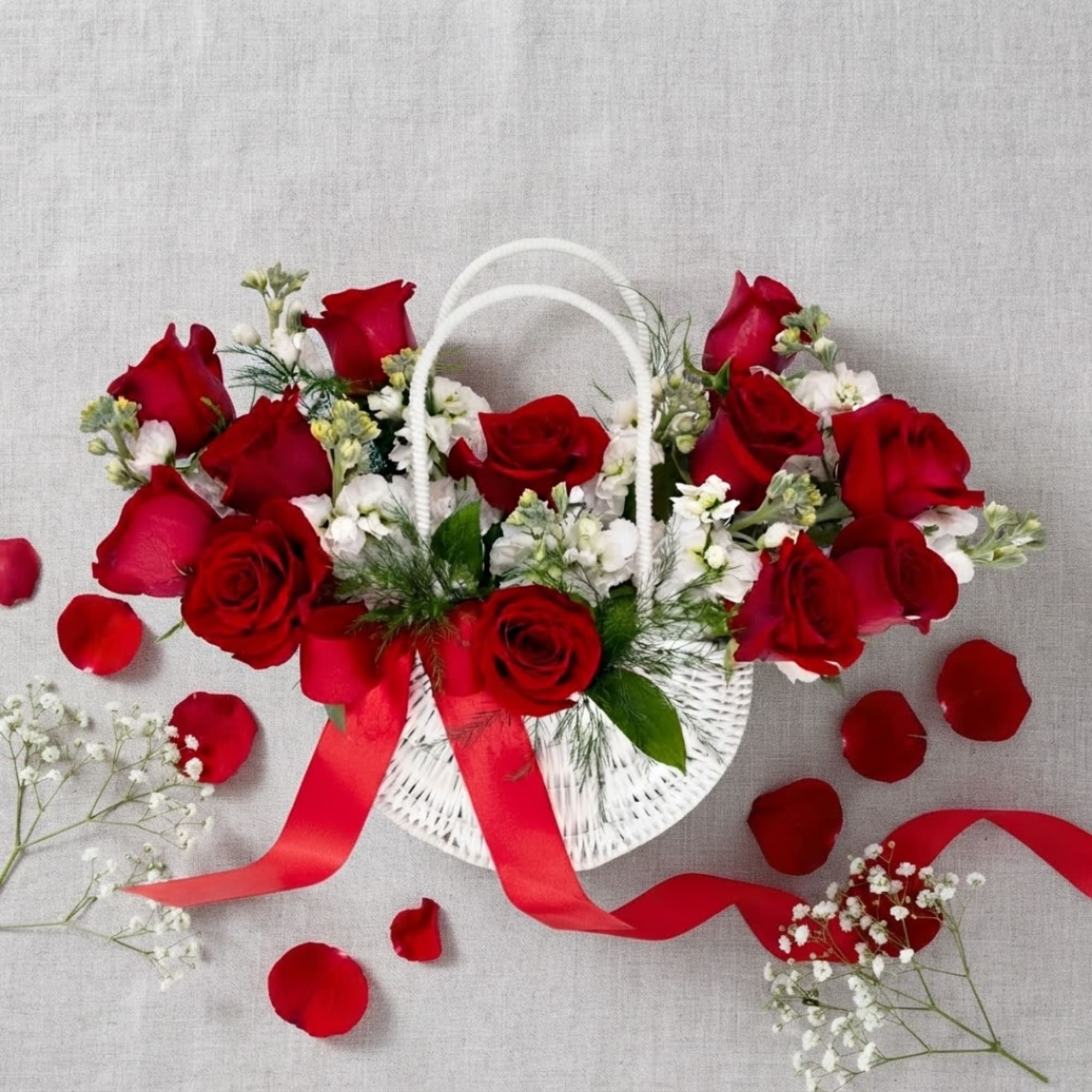 Red roses and white filler flowers in a white basket with a red ribbon