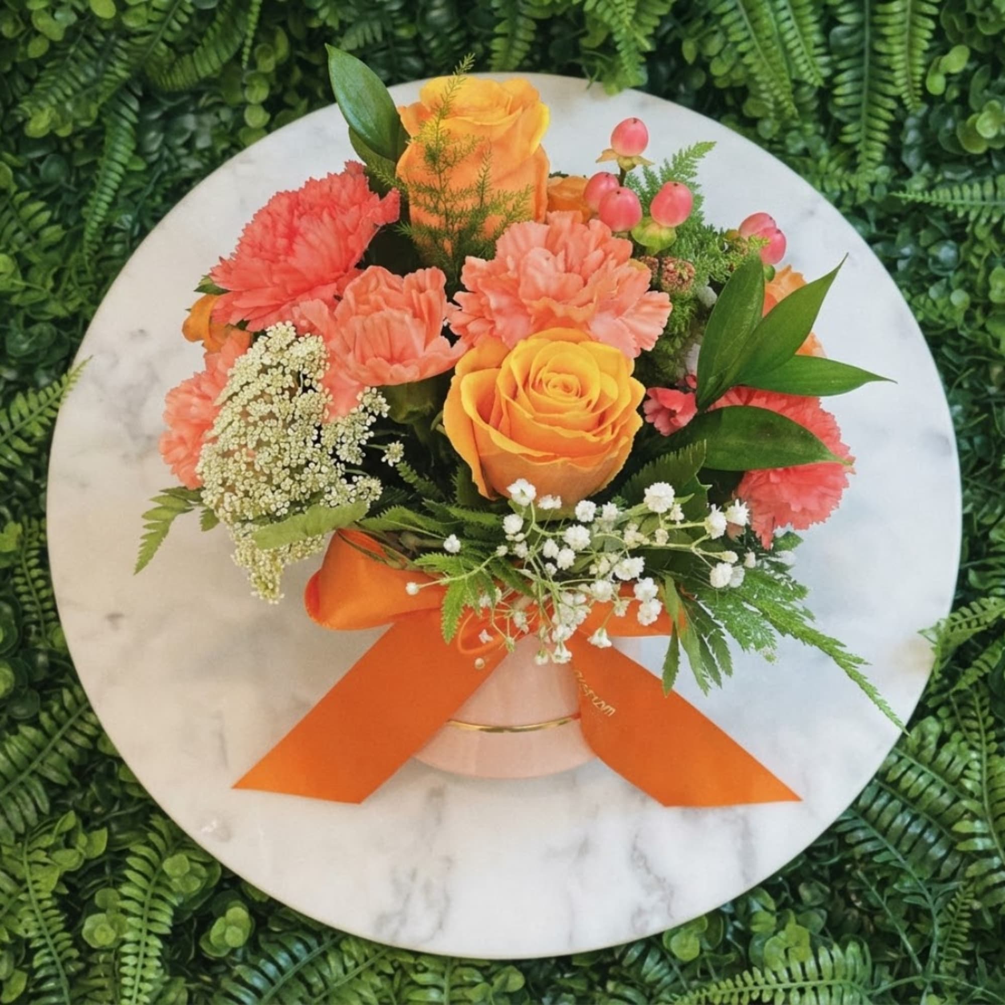 Orange and coral bouquet in a pink vase with a ribbon