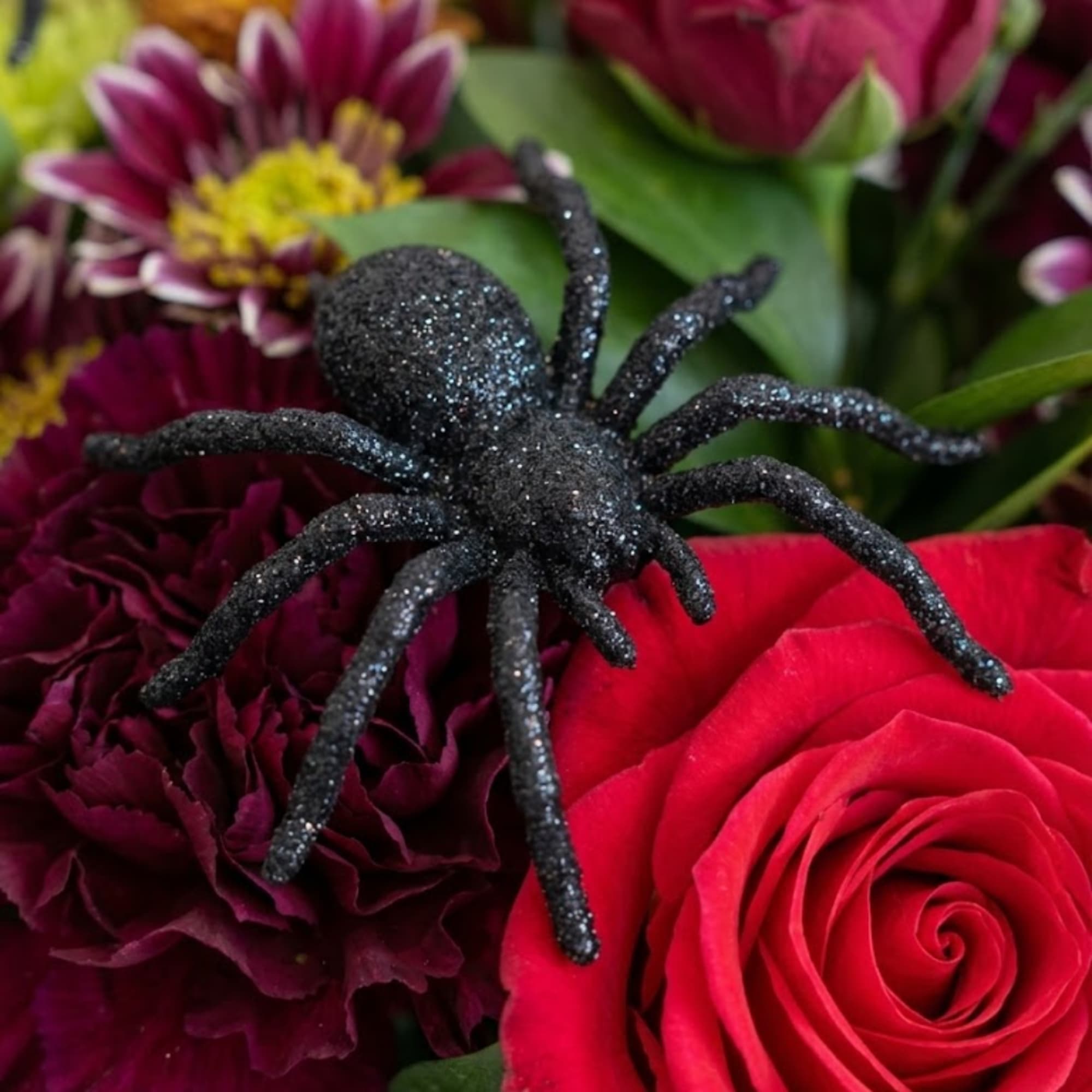 Bouquet with a glittery black spider decoration over red and purple flowers