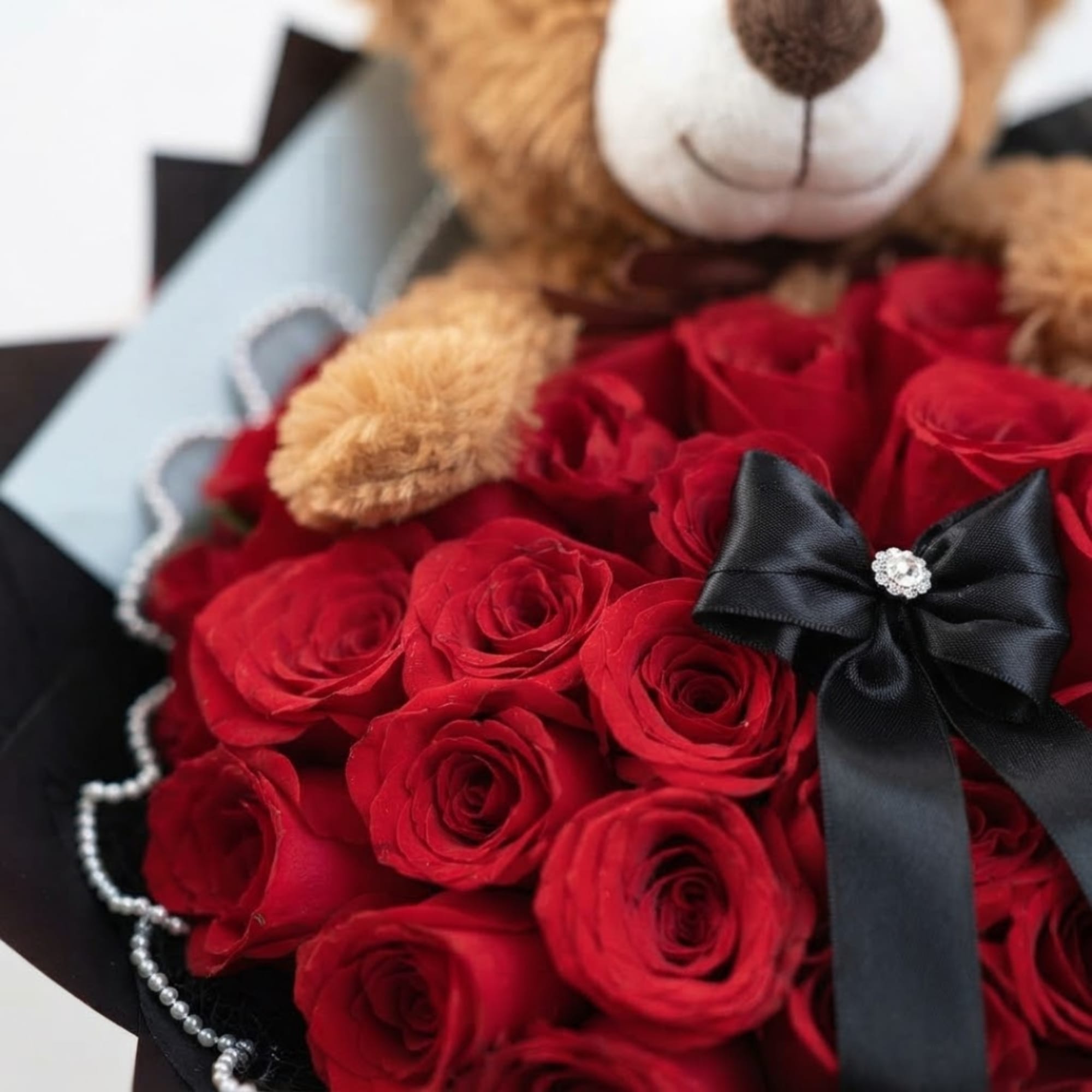 Red roses arranged with a teddy bear and black ribbon