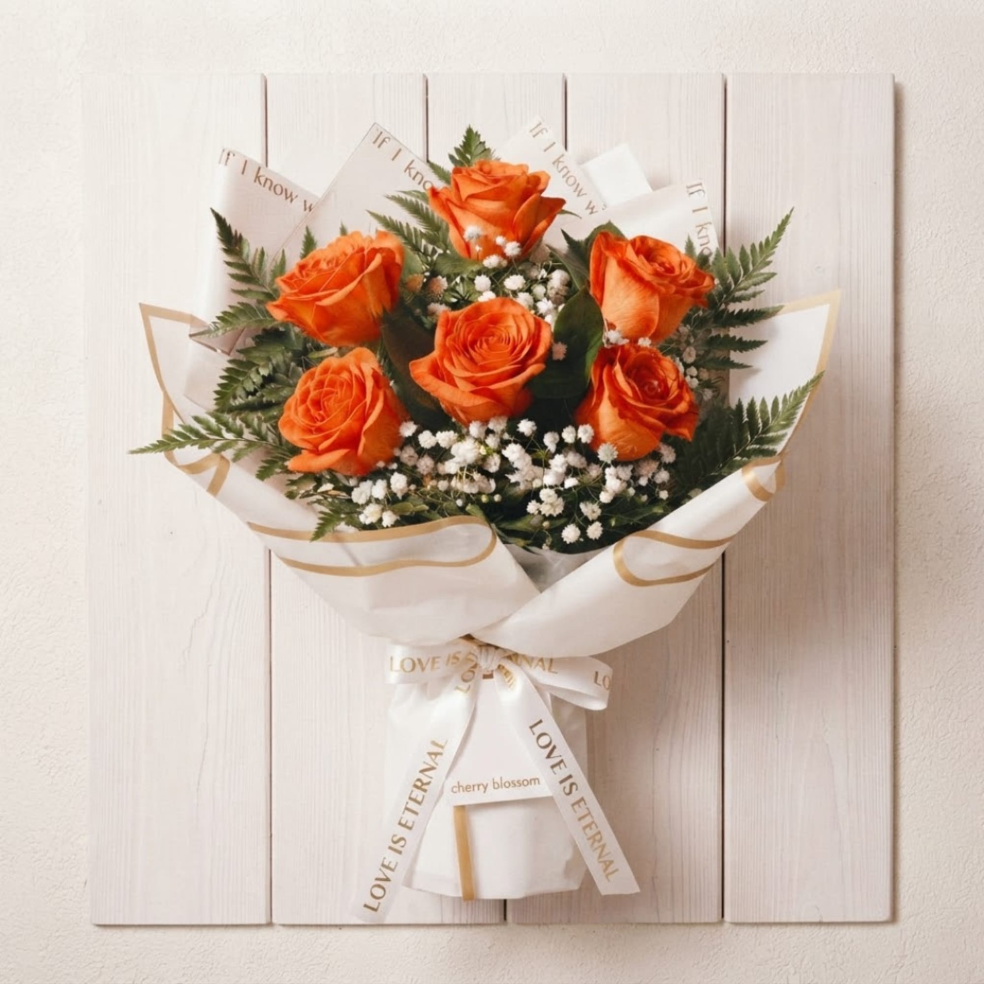 Orange roses in a wrapped bouquet with white filler flowers