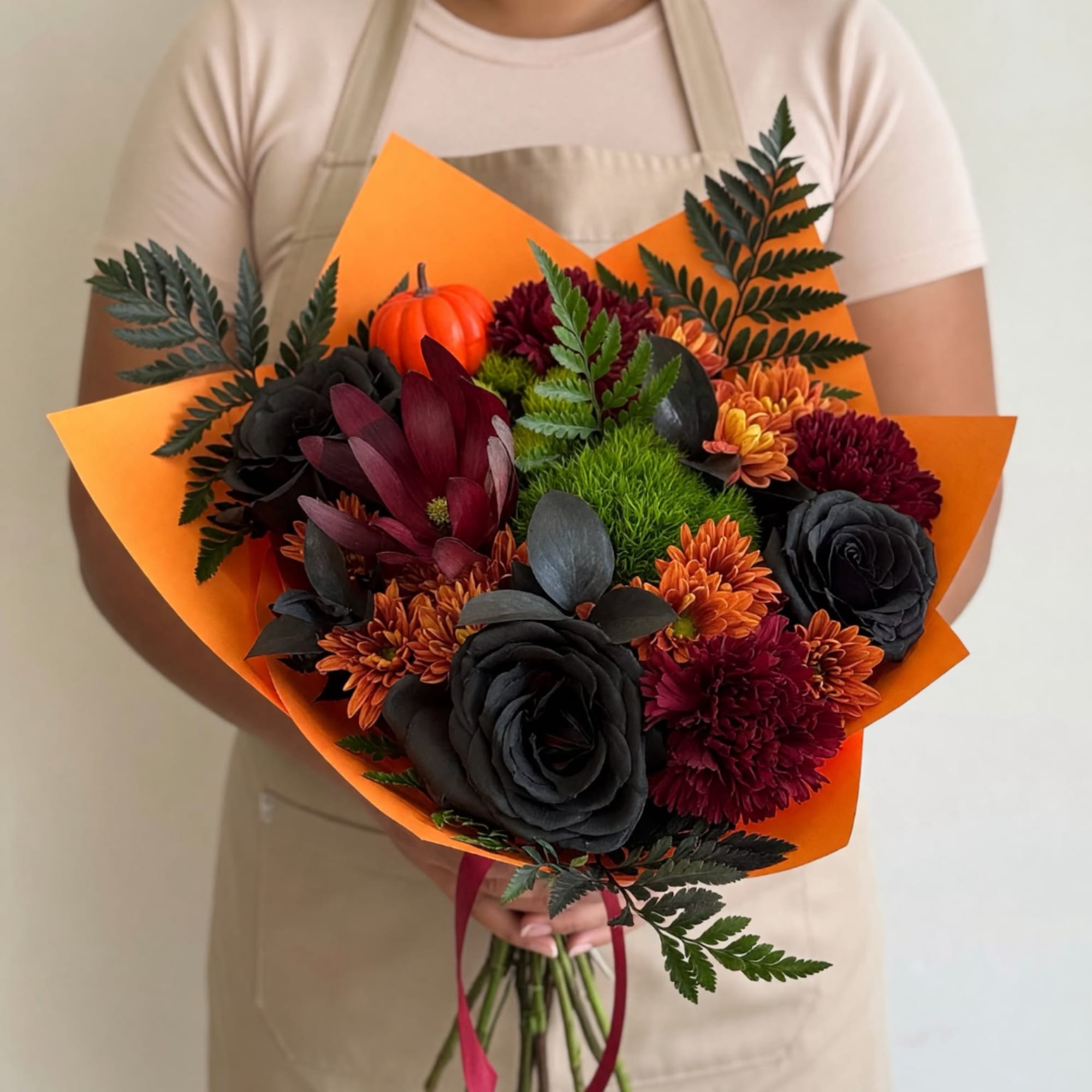 Handheld bouquet of dark flowers wrapped in bright orange paper, photo 2 of 5