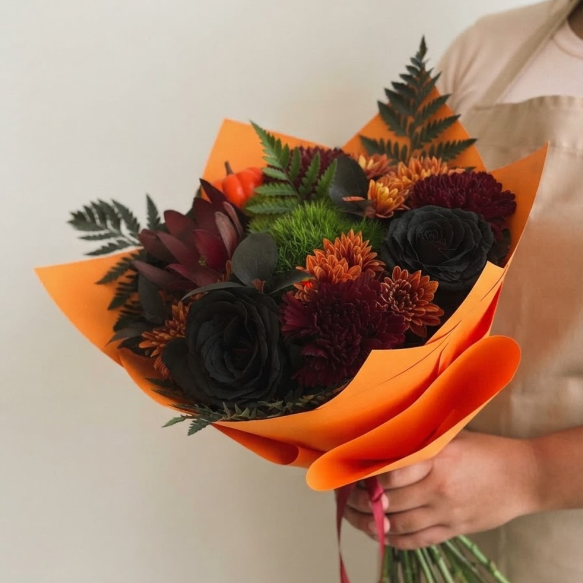 Handheld bouquet of dark flowers wrapped in bright orange paper, photo 3 of 5