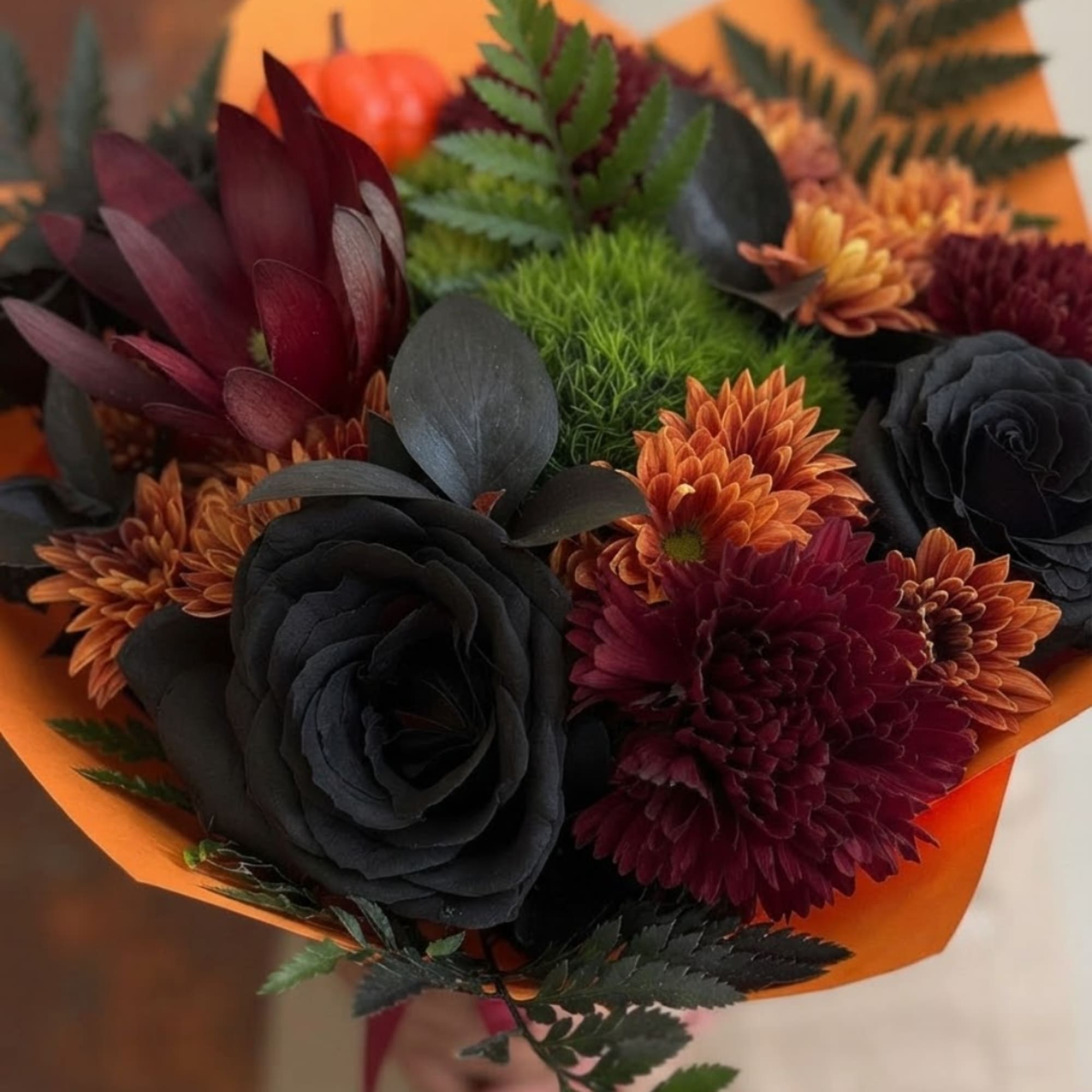 Bouquet of dark roses and orange chrysanthemums wrapped in orange paper