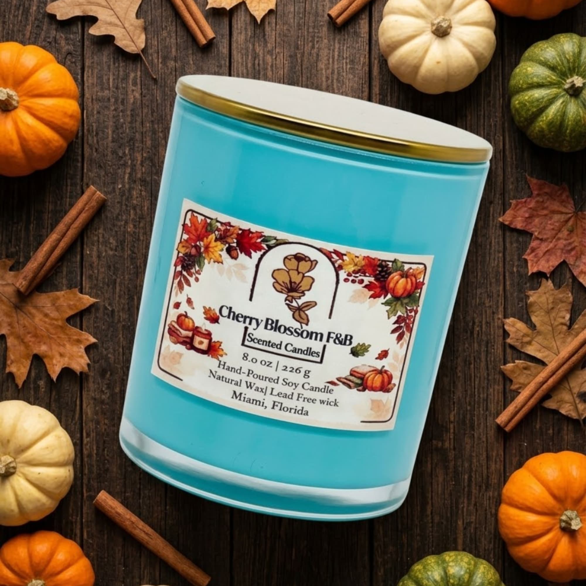 Blue scented candle in a glass jar surrounded by pumpkins and cinnamon sticks