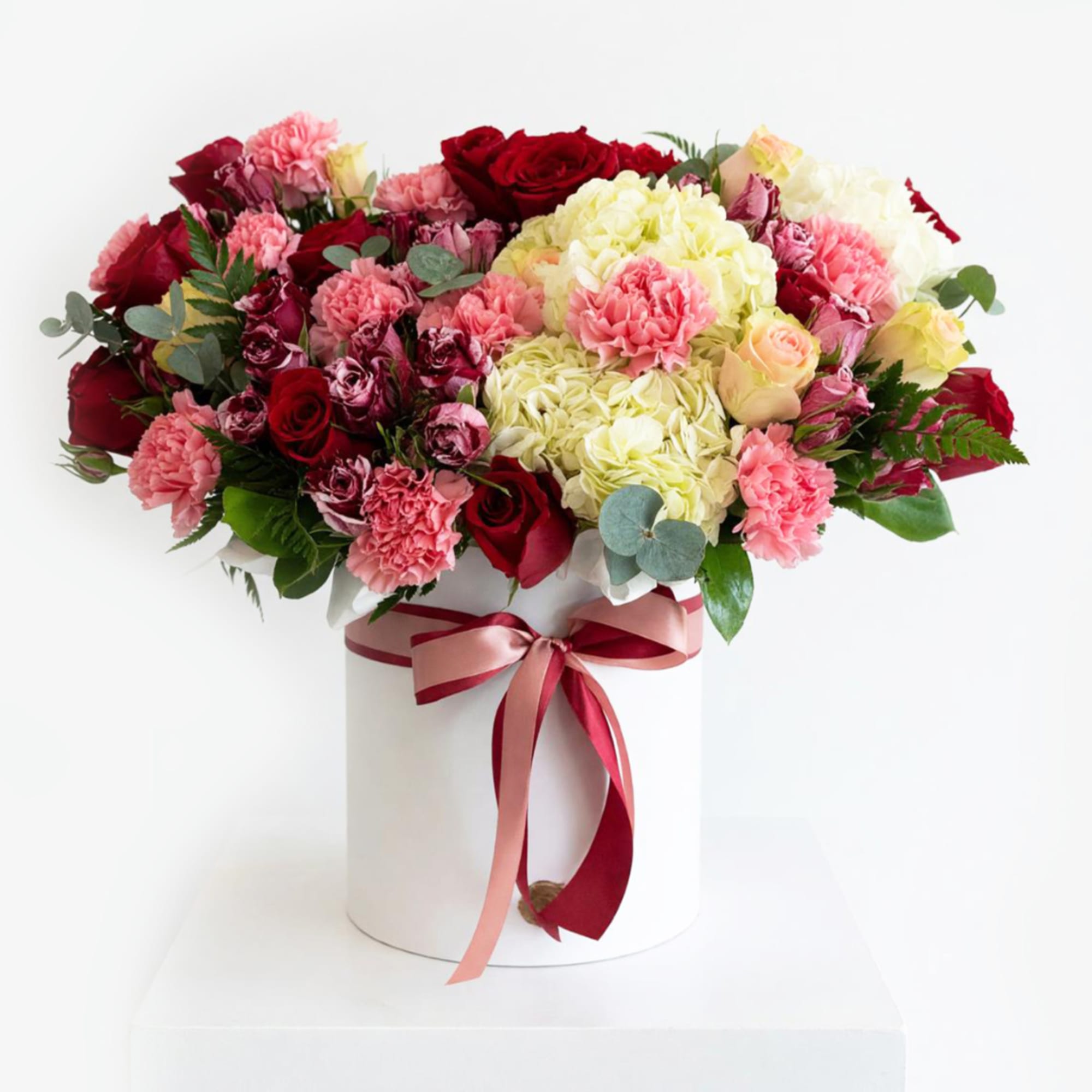 Bouquet of red, pink, and cream flowers in a white hatbox with ribbon