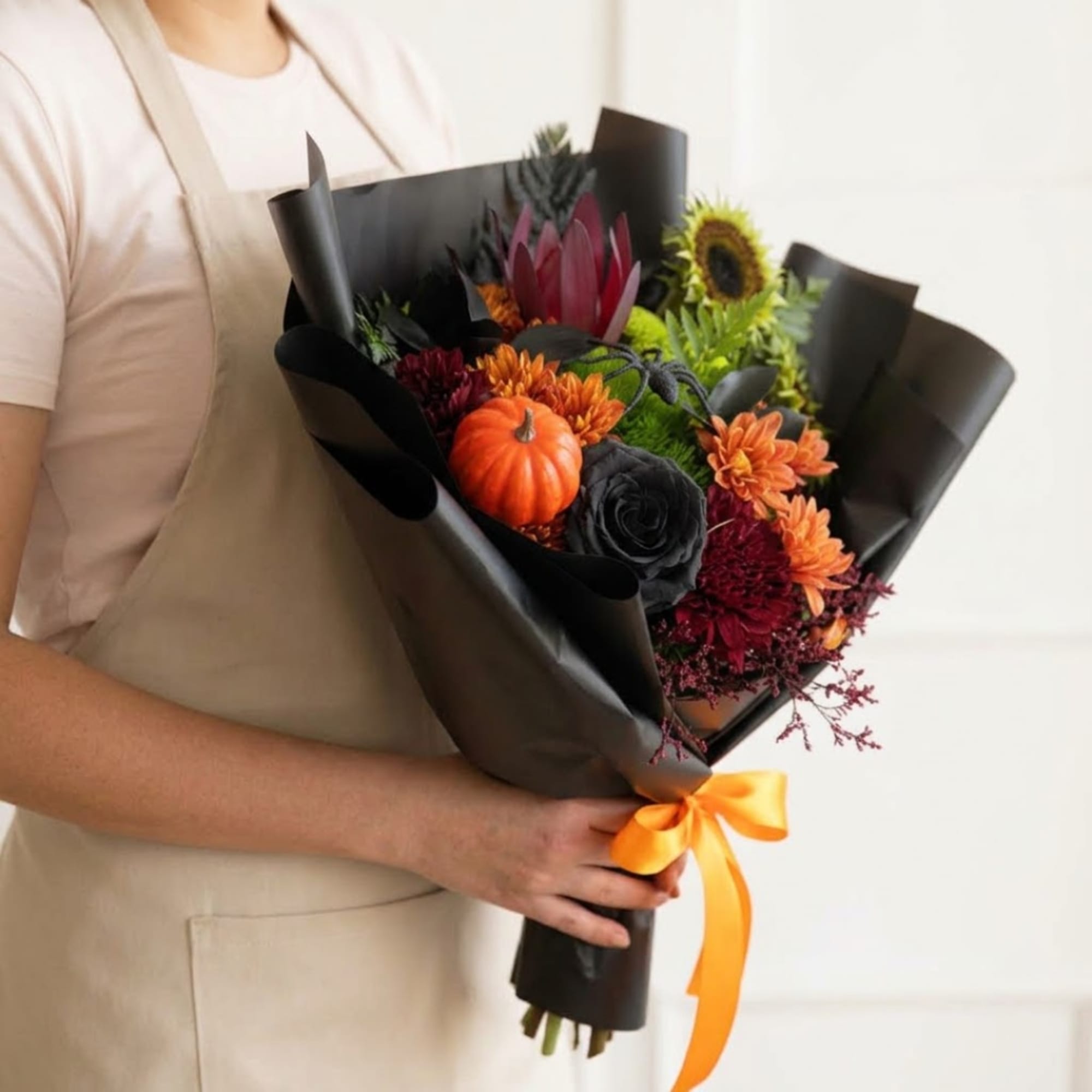 Person holding a bouquet with a small pumpkin and orange, burgundy, and black flowers