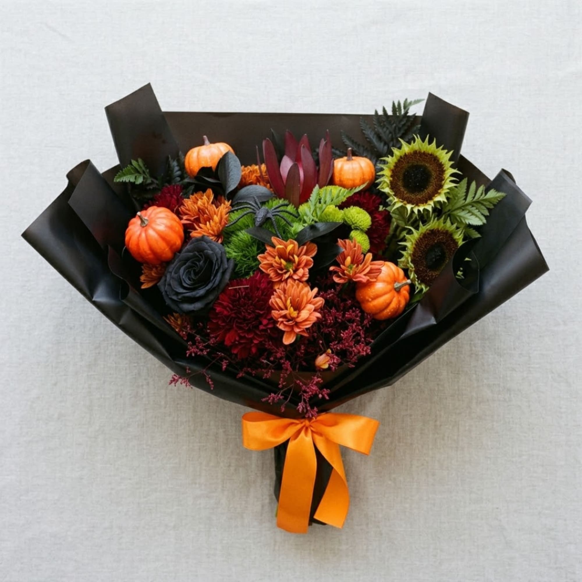 Autumn bouquet with sunflowers, orange blooms, and small pumpkins wrapped in black paper