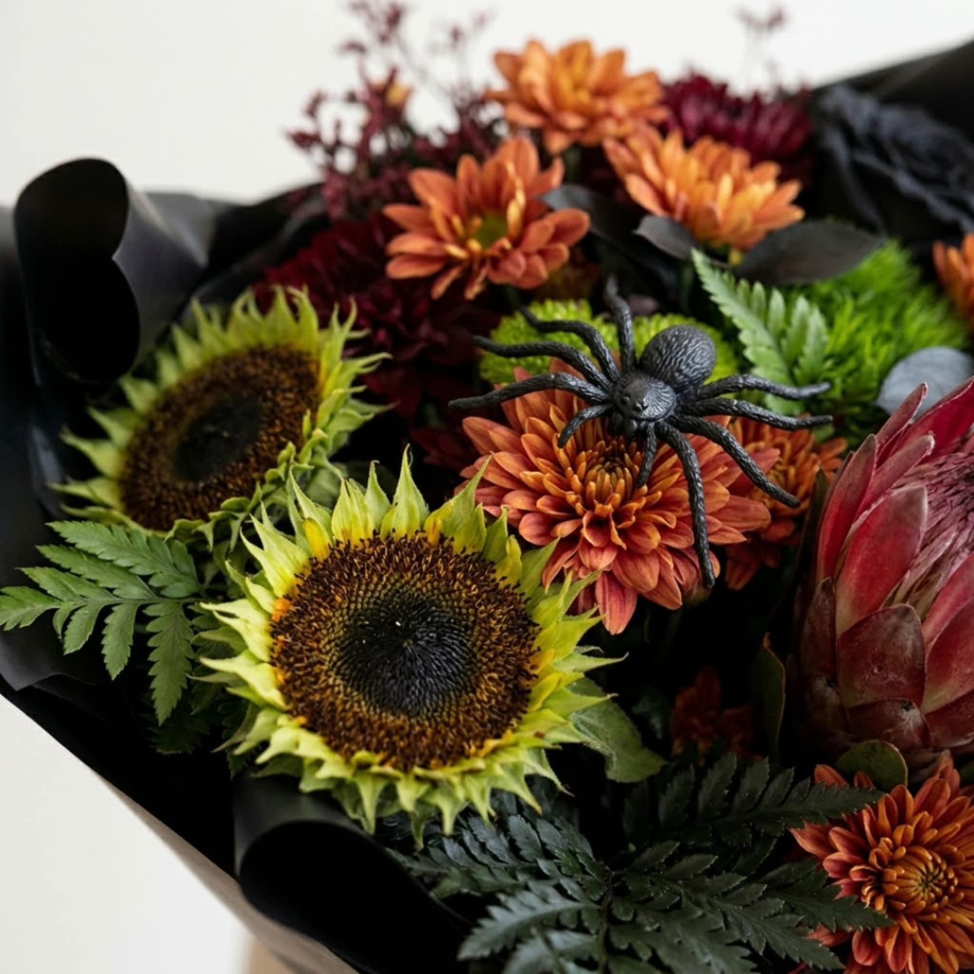 Bouquet of sunflowers, orange mums, and a black spider decoration wrapped in black paper