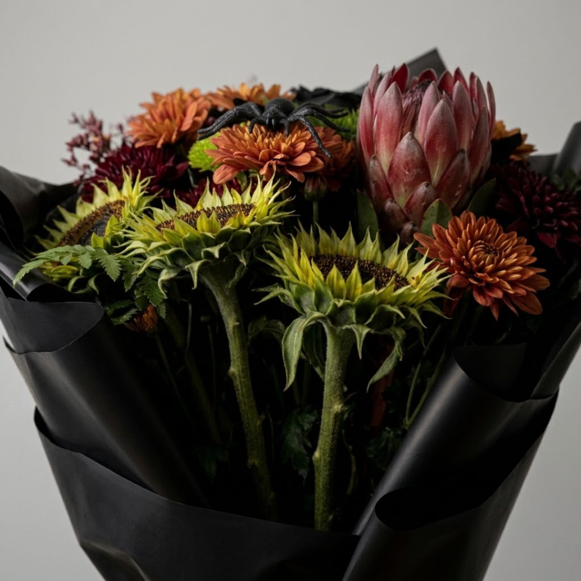 Bouquet of sunflowers, orange mums, and a pink protea wrapped in black paper