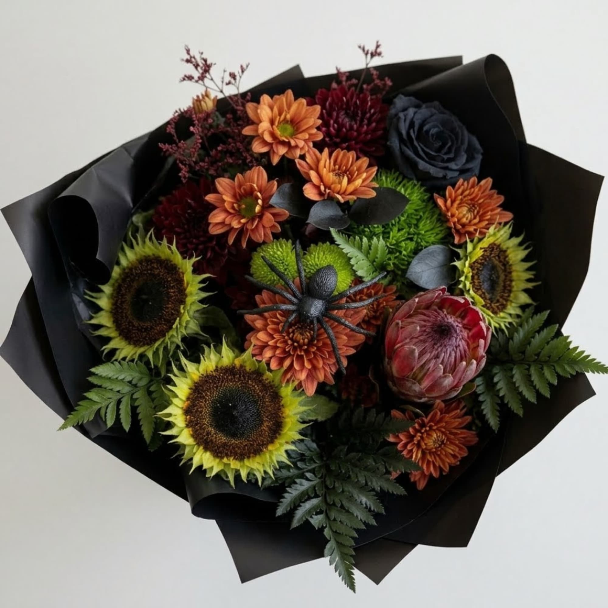 Bouquet of sunflowers, orange mums, and a protea wrapped in black paper