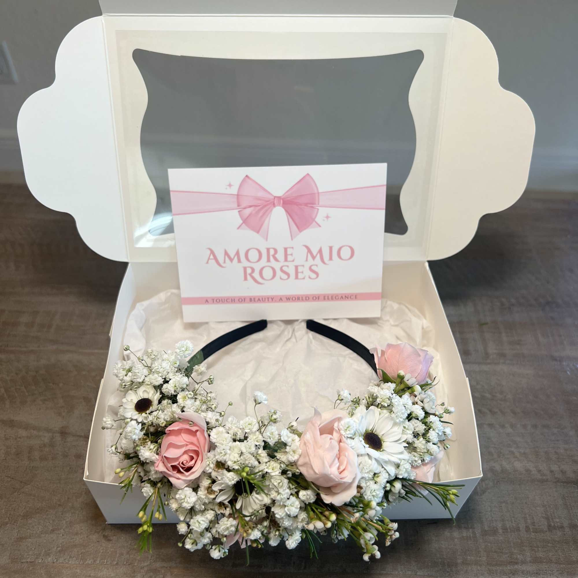 Pink roses and white daisies arranged in a gift box with a ribbon card