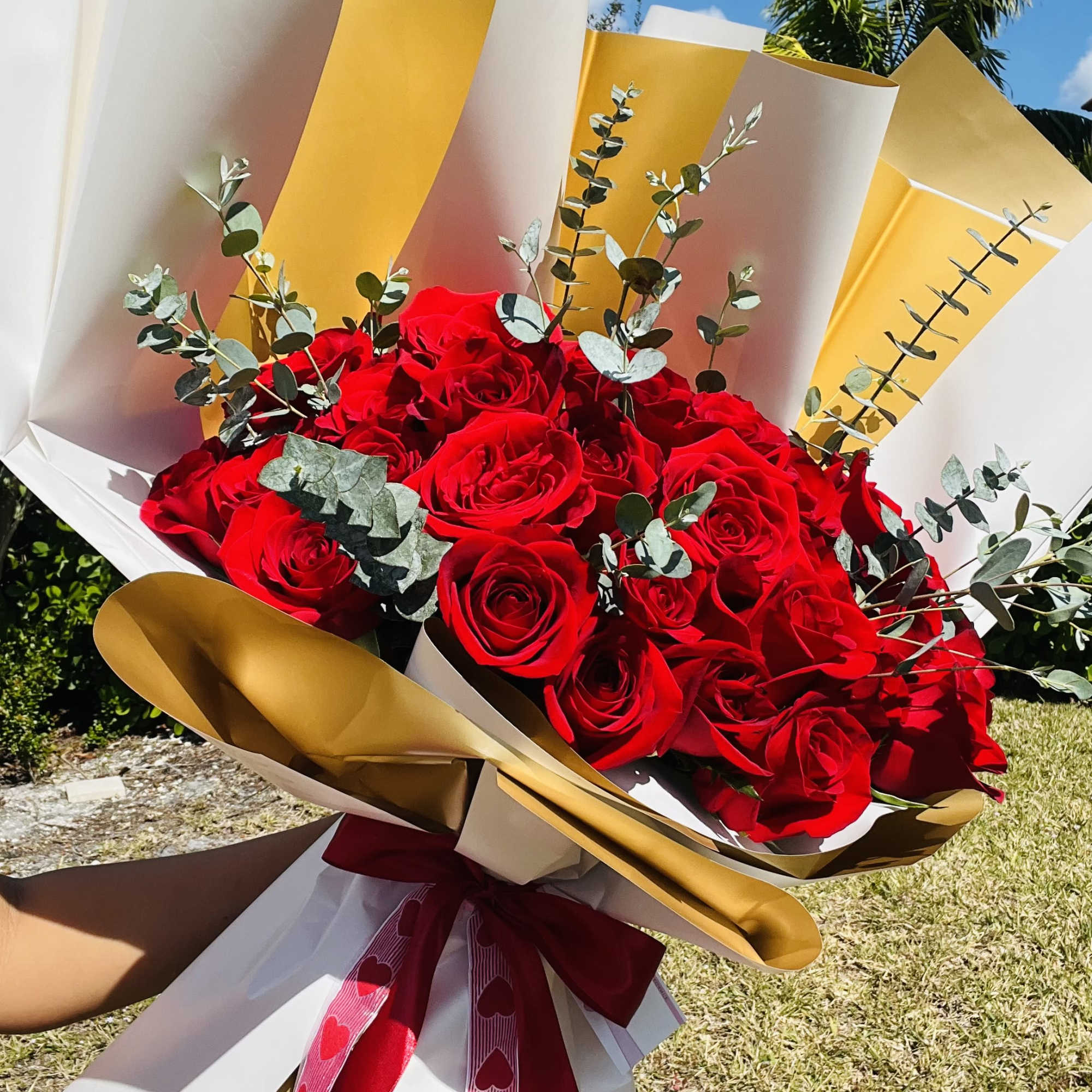 Bouquet of red roses wrapped in white and gold paper with a heart ribbon