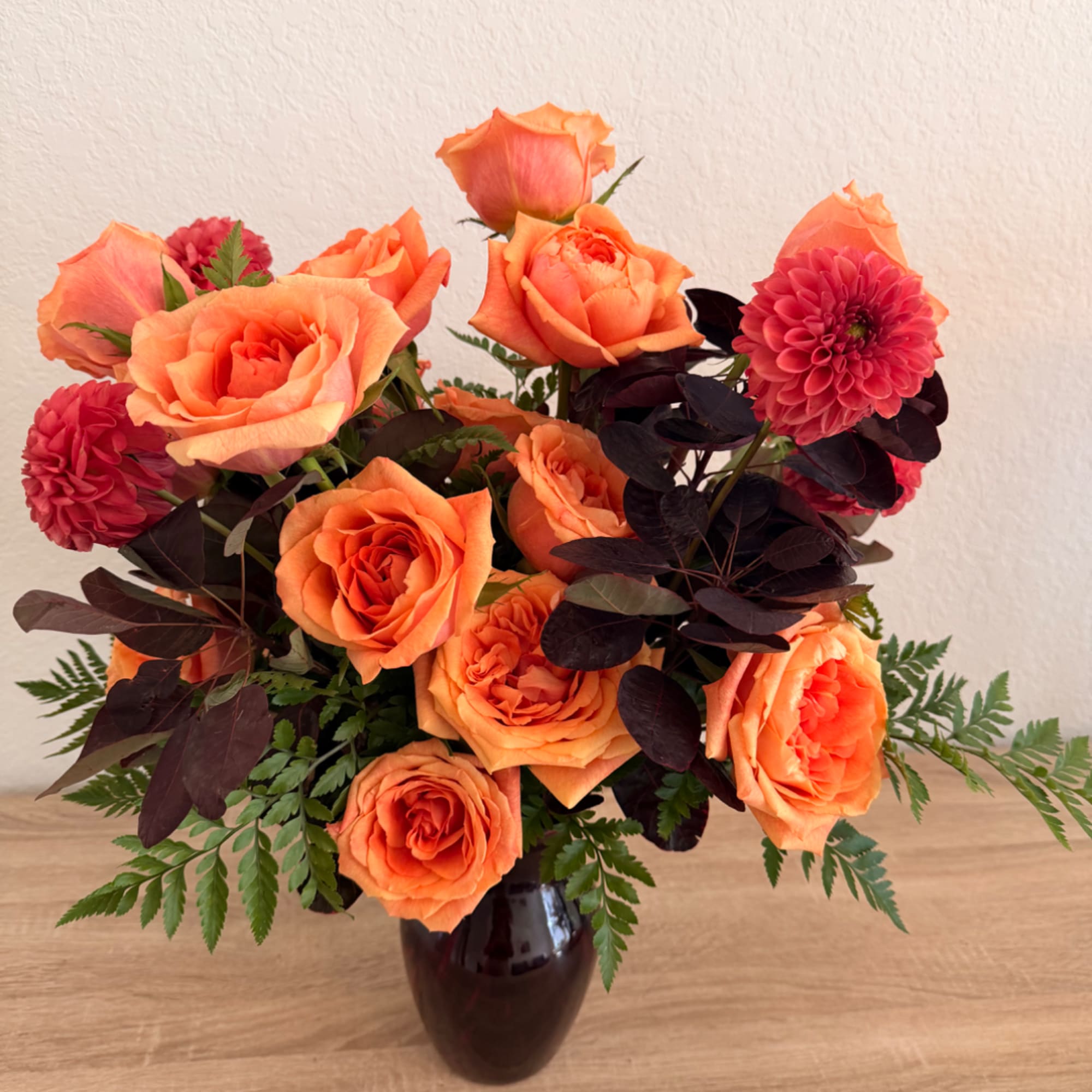 Orange roses and pink dahlias in a dark vase