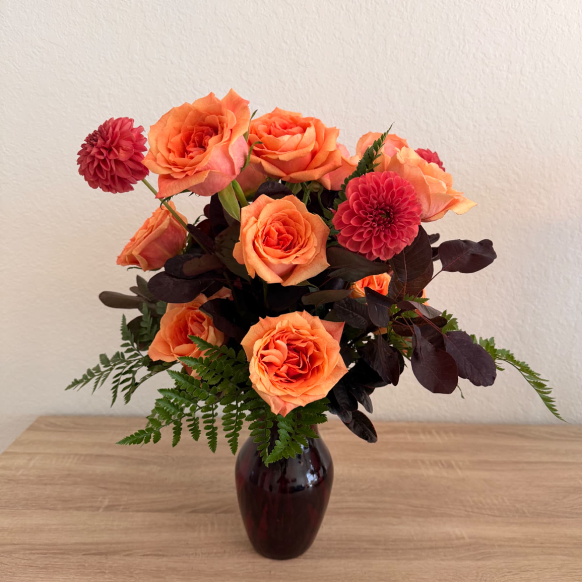 Orange roses and pink dahlias in a dark glass vase