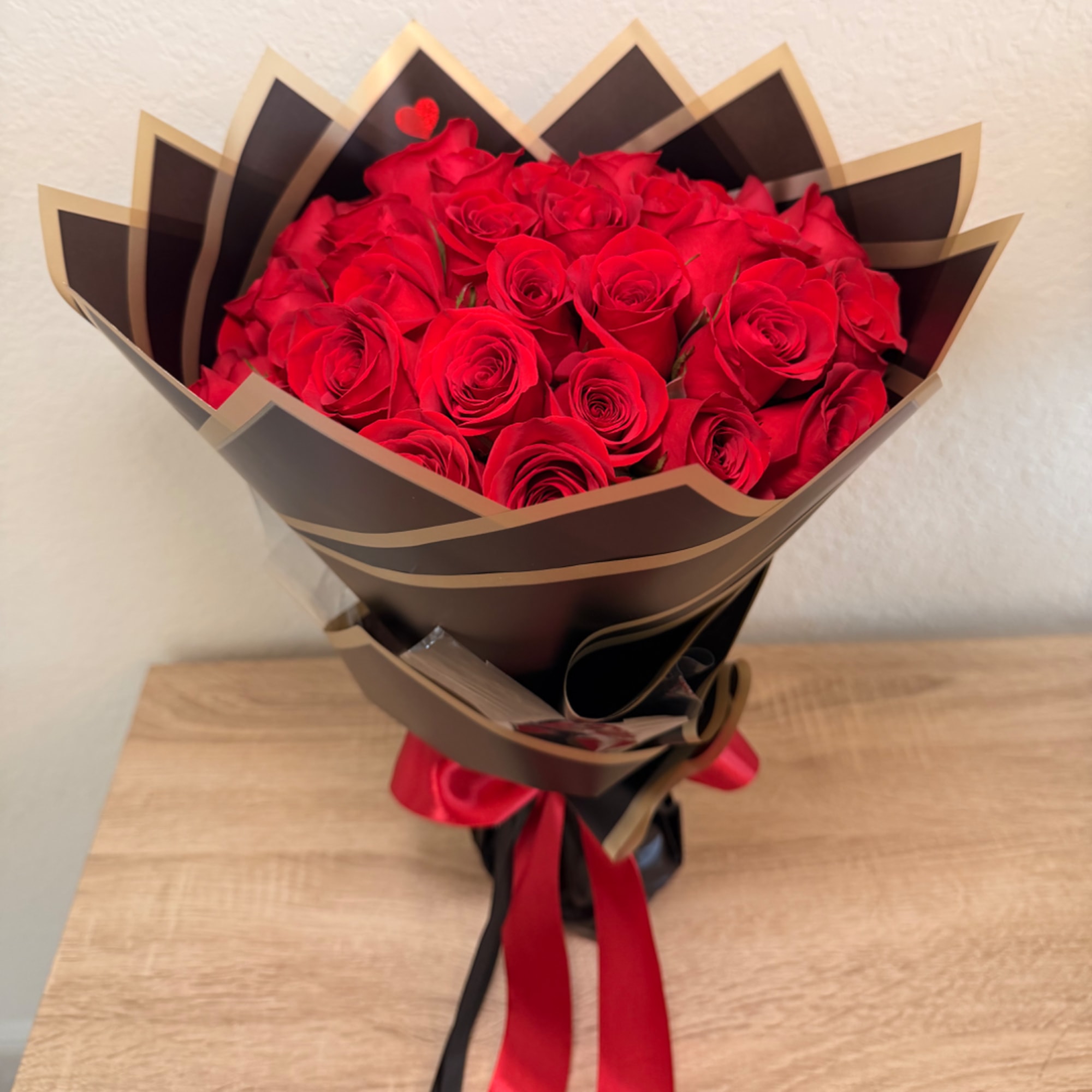 Bouquet of red roses wrapped in dark paper with a red ribbon
