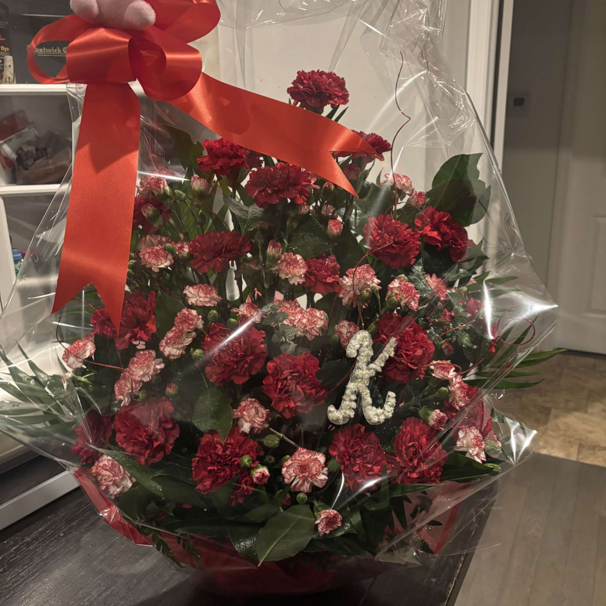 Wrapped bouquet of red and pink carnations with a red ribbon and plush teddy bear