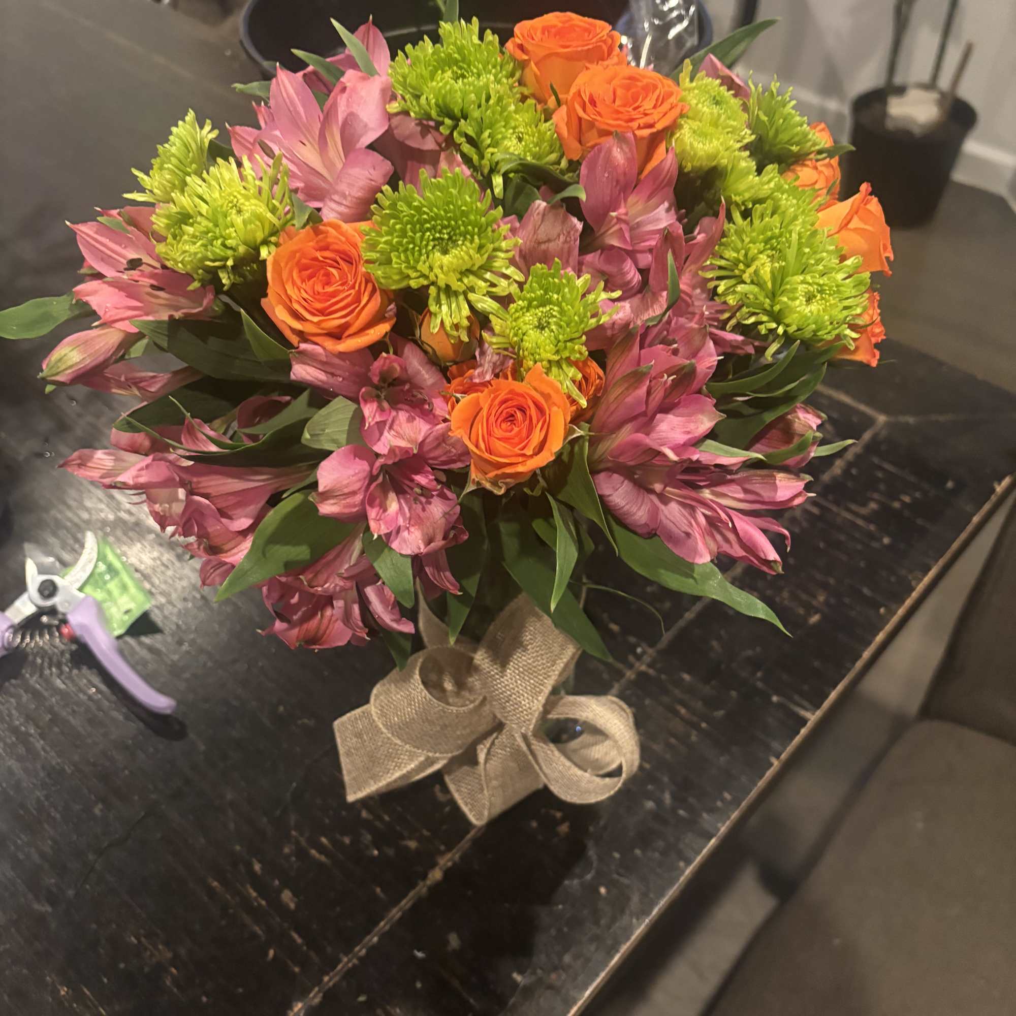 Bouquet of orange roses, pink alstroemeria, and green chrysanthemums tied with burlap ribbon