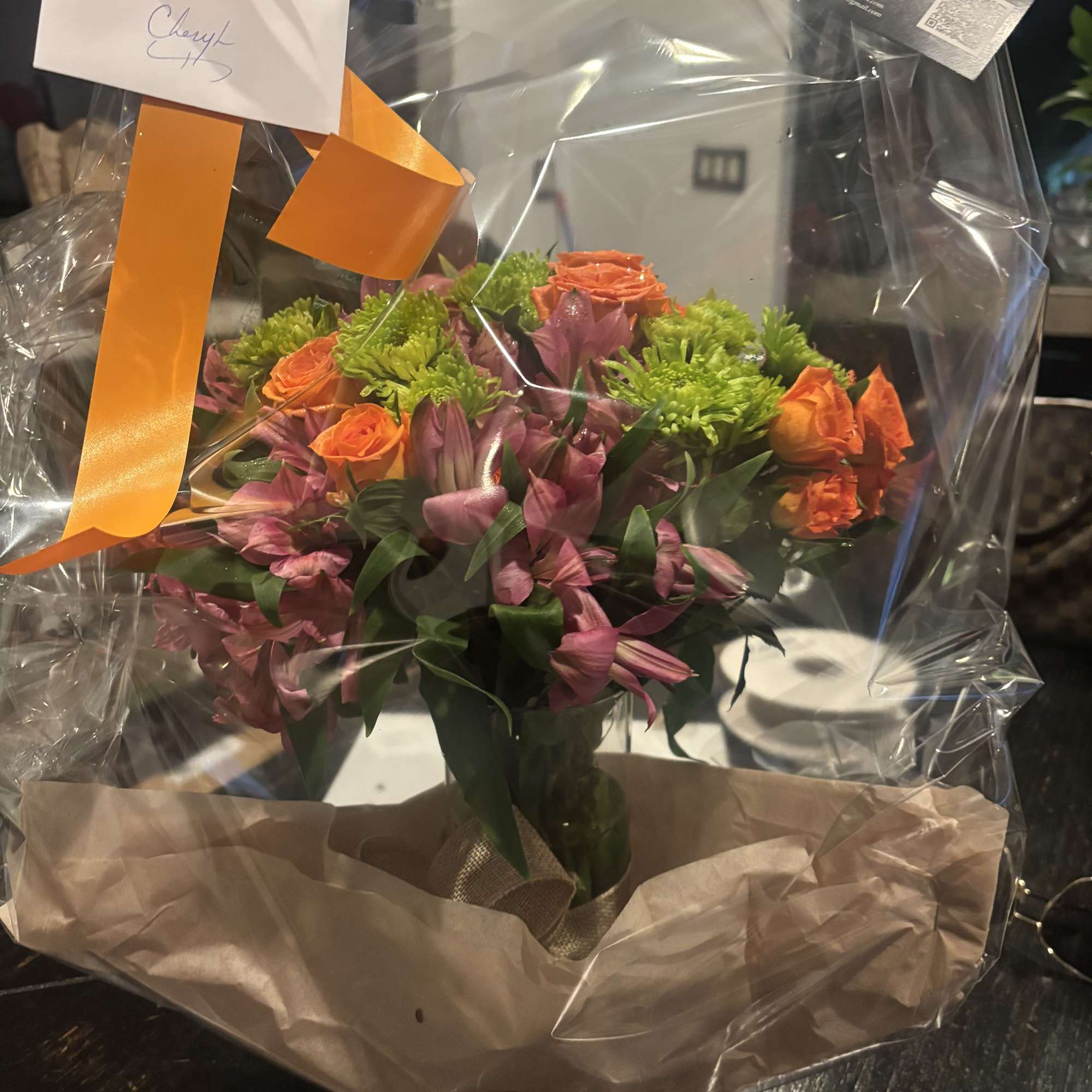 Bouquet of orange roses and pink flowers wrapped in clear plastic with an orange ribbon.