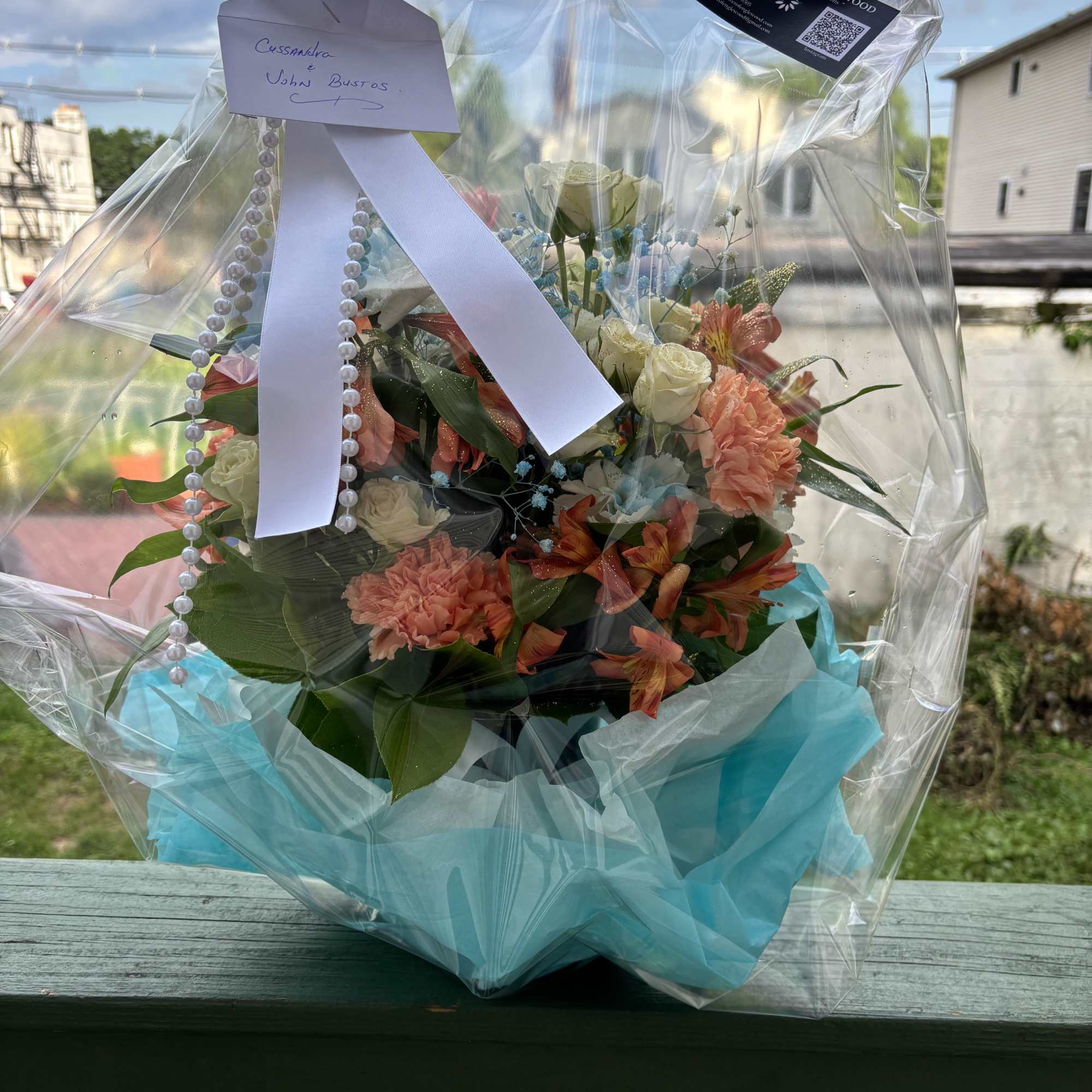 Wrapped bouquet of mixed flowers with a white ribbon and pearl strands