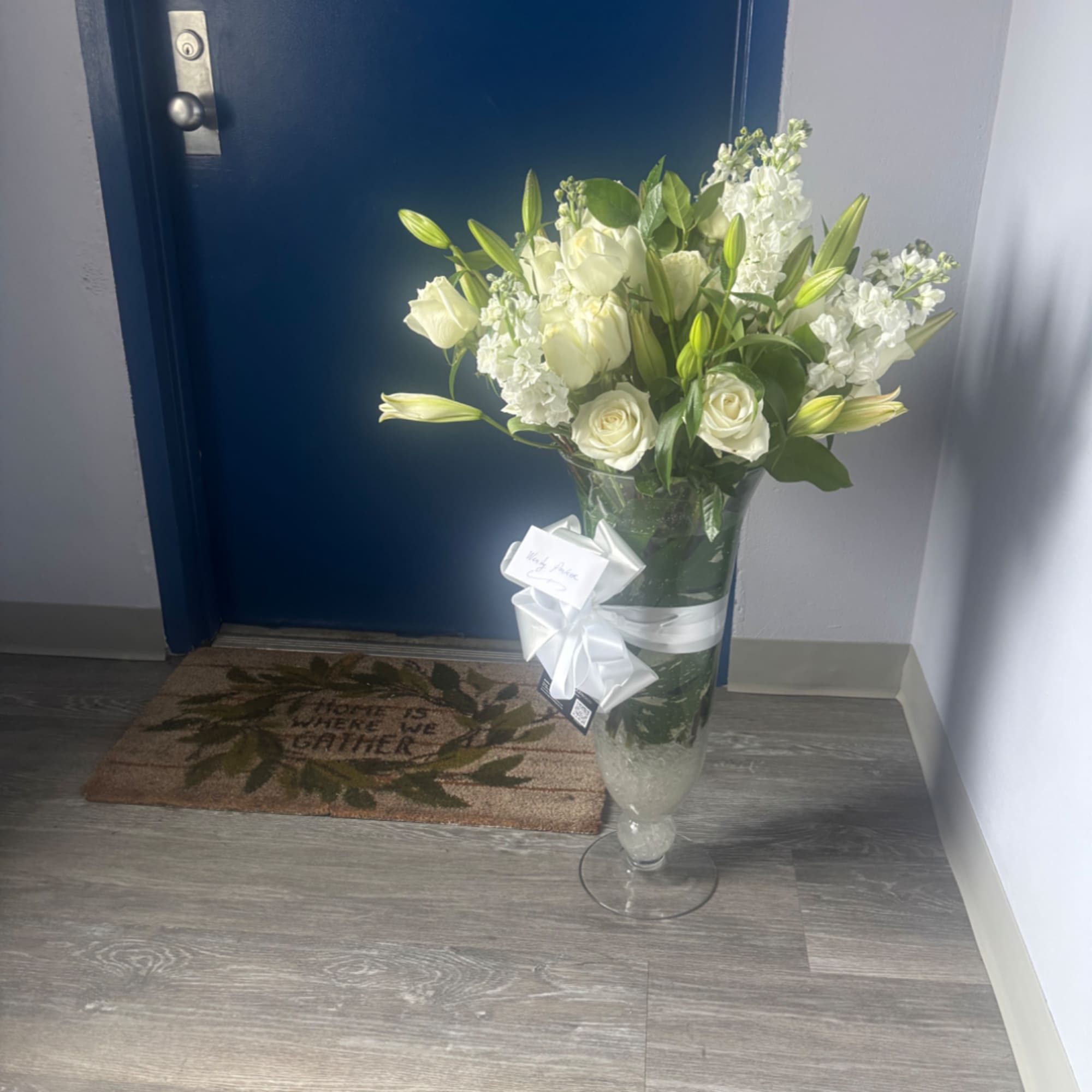 White roses and lilies arranged in a tall glass vase with a white ribbon., photo 2 of 2