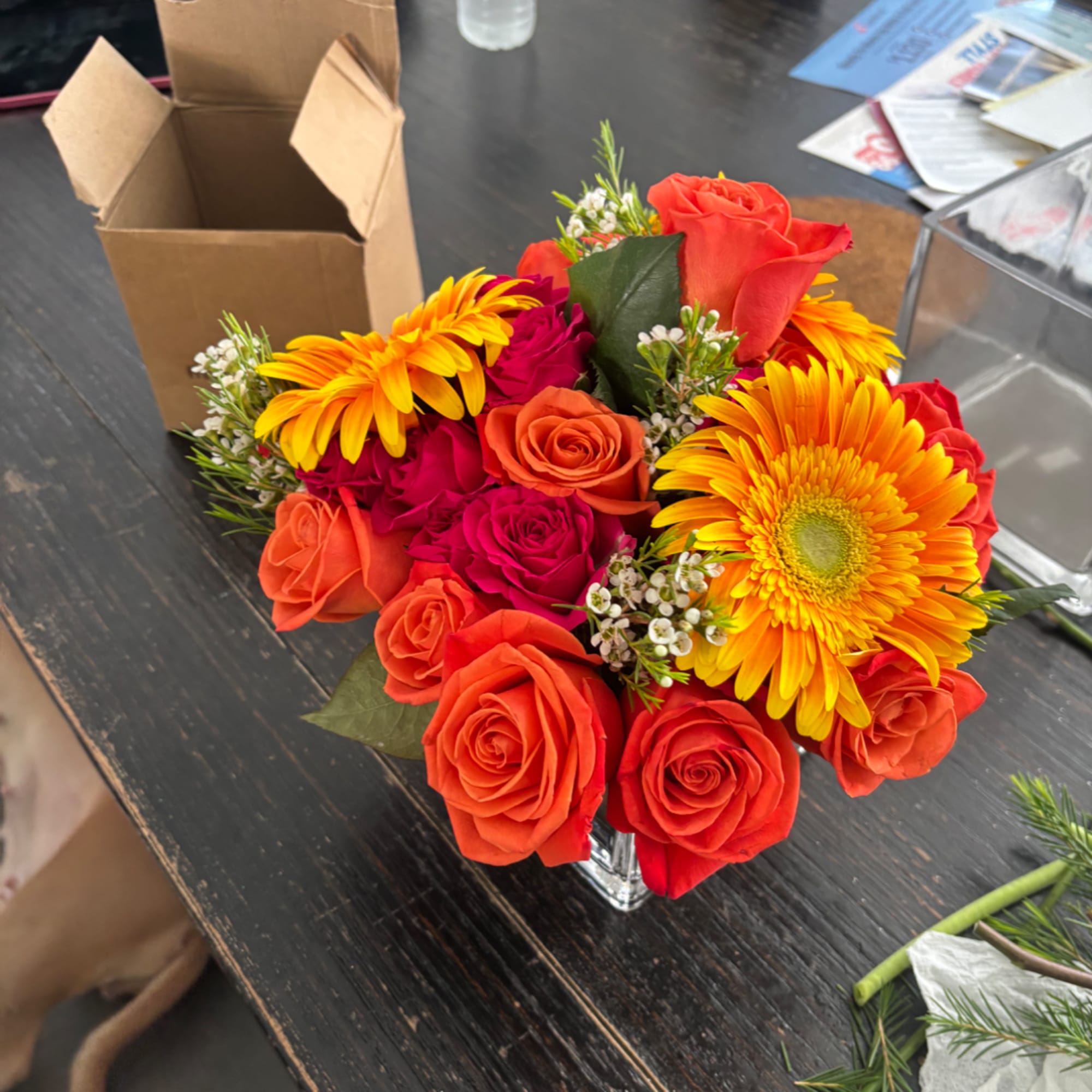 Bouquet of orange and red roses with yellow gerbera daisies in a clear vase
