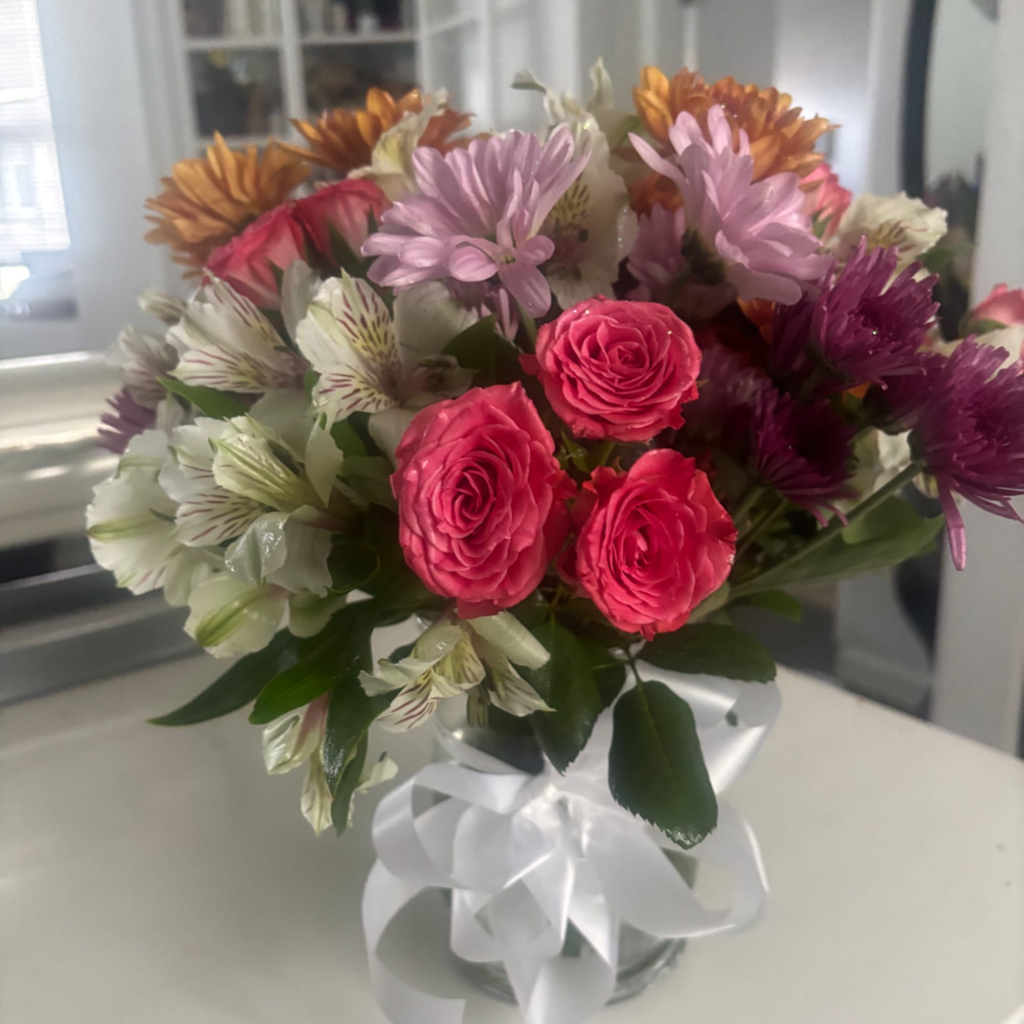 Mixed bouquet of pink roses and daisies in a glass vase with a white ribbon