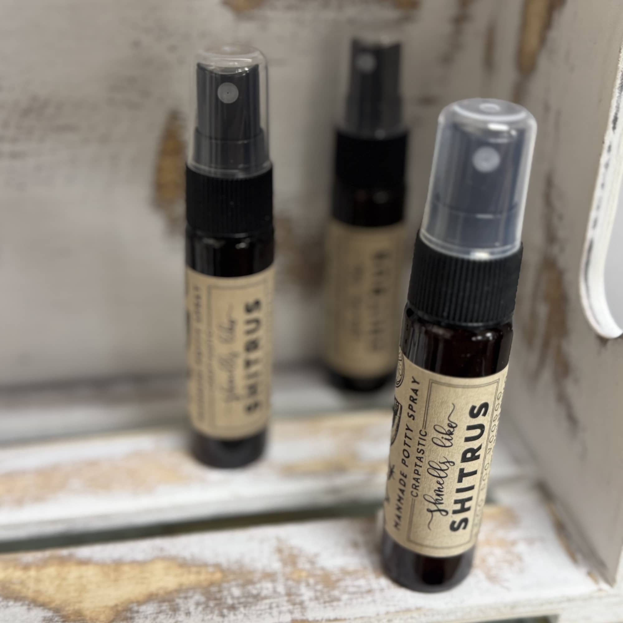 Three small spray bottles labeled Shitrus sit in a distressed wooden tray.