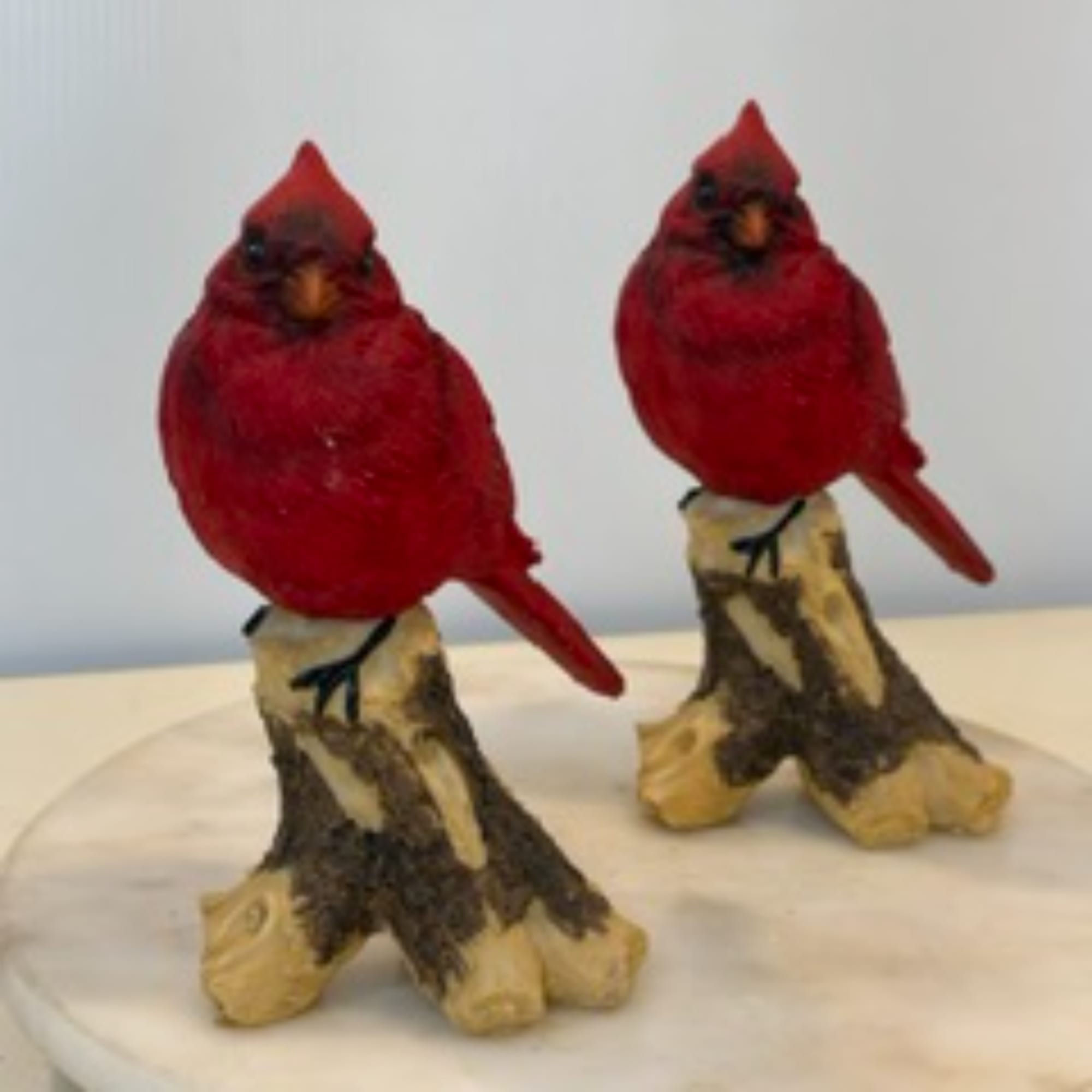 Two red bird figurines perched on small wood stumps