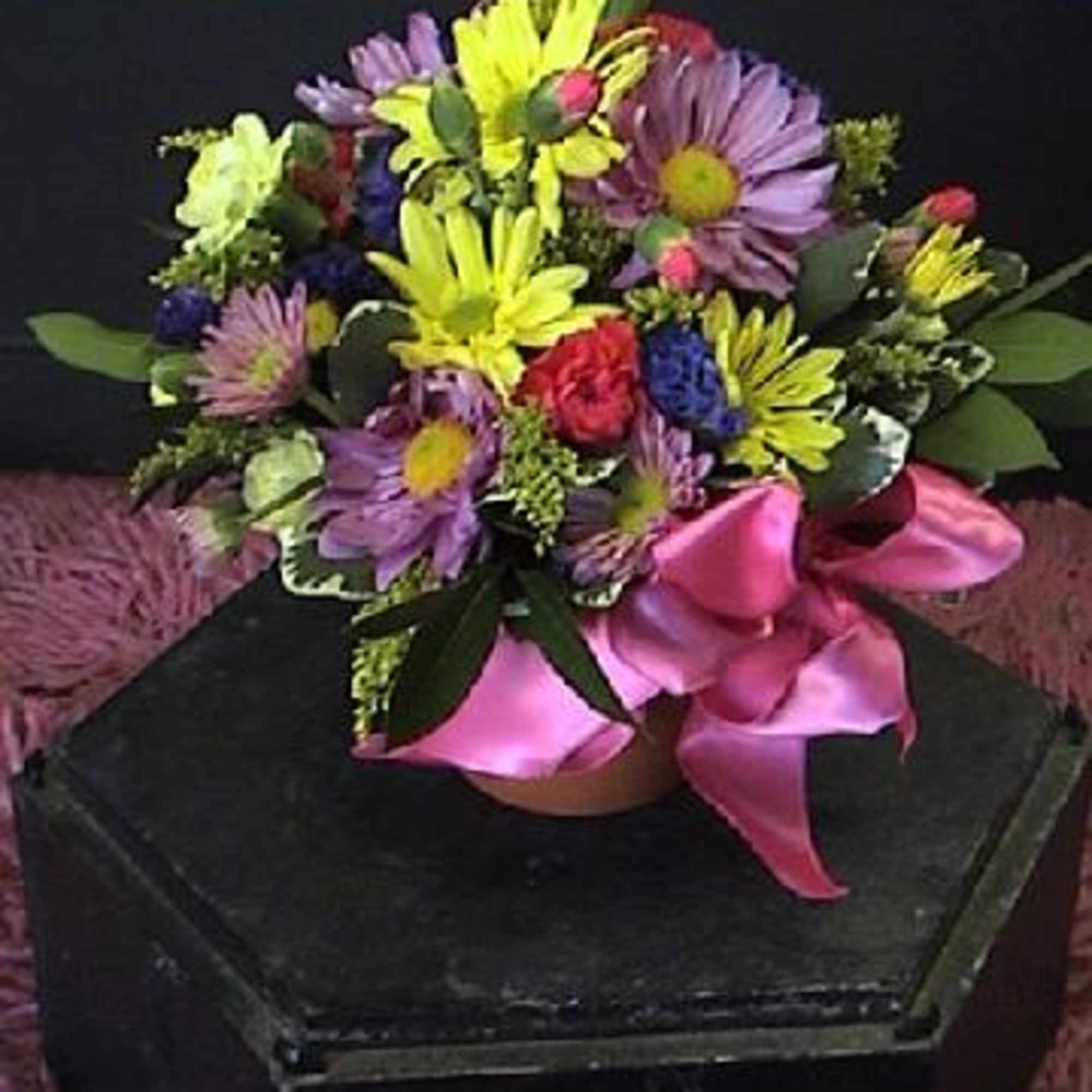 Mixed bouquet of purple, yellow, and pink flowers with a pink ribbon