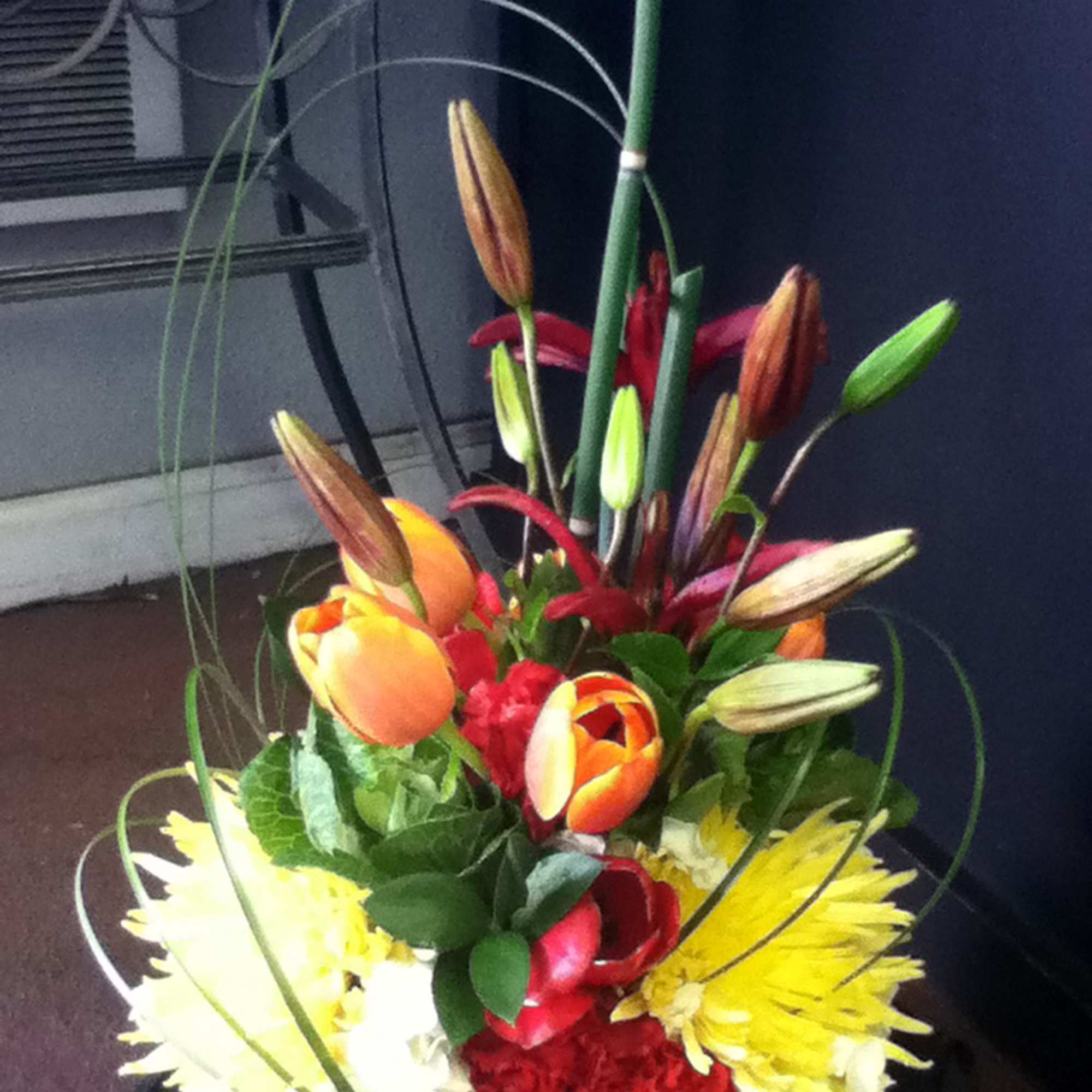 Tall bouquet of lilies, tulips, and chrysanthemums in bright red, yellow, and orange
