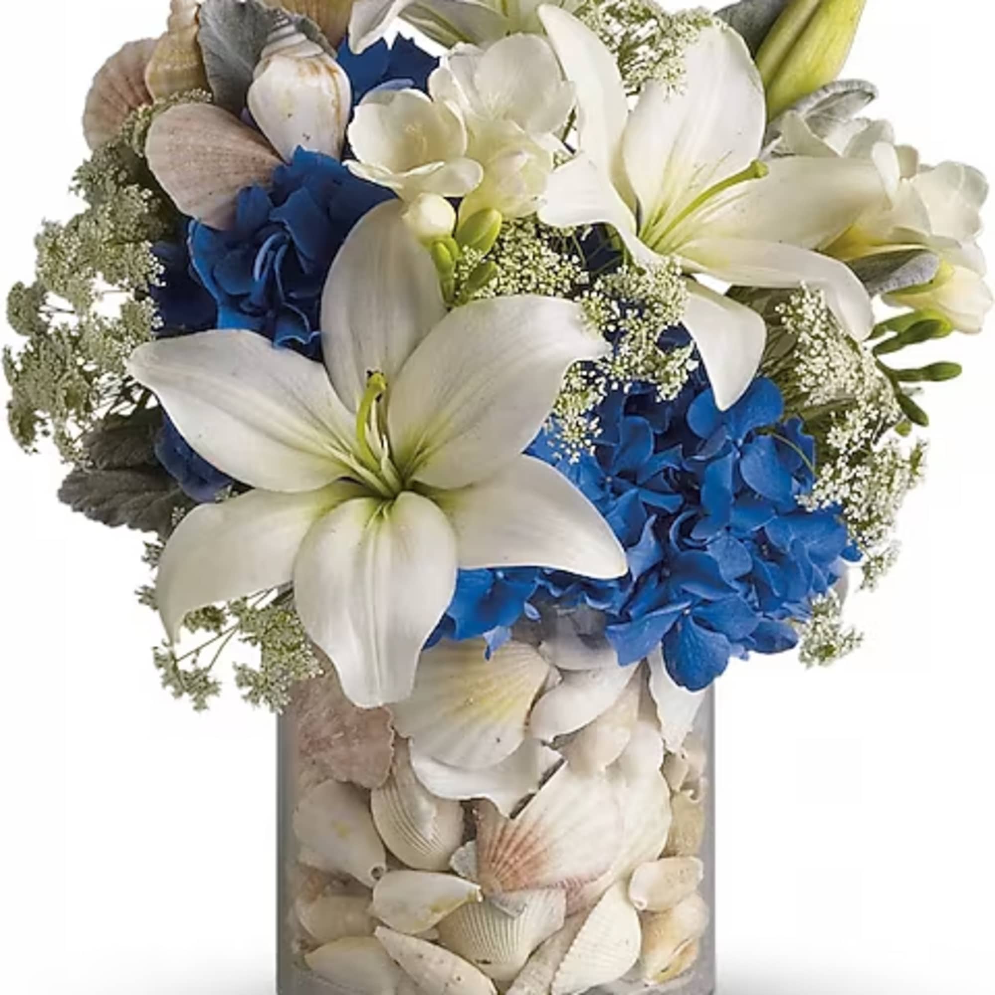 White lilies and blue hydrangeas in a shell-filled glass vase