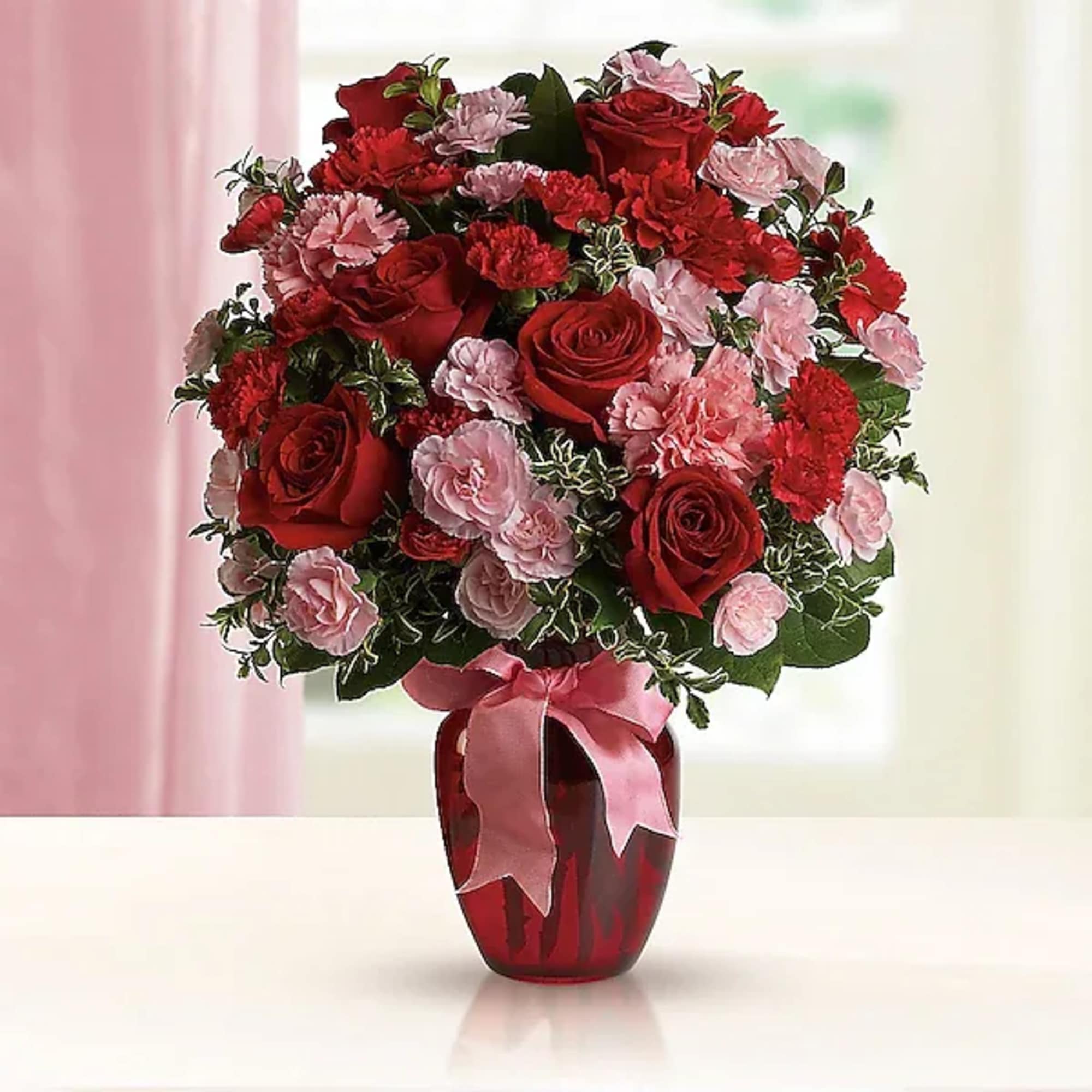 Red roses and pink carnations in a red vase with a pink ribbon
