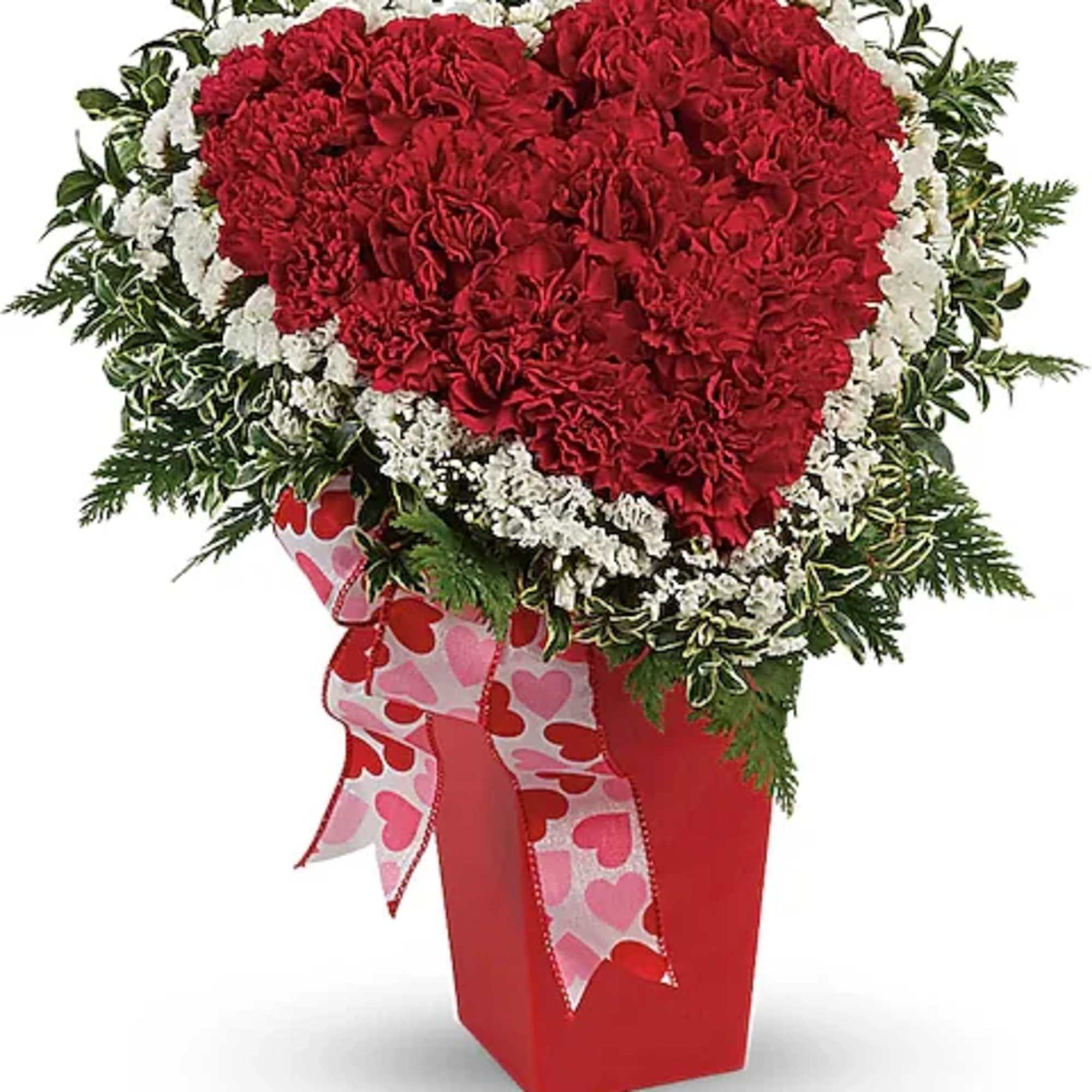 Heart-shaped red carnation arrangement in a red vase with heart ribbon