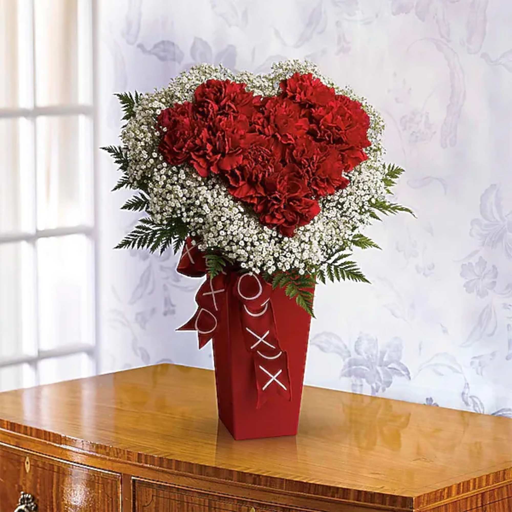Heart-shaped red carnation arrangement in a red vase with white baby's breath