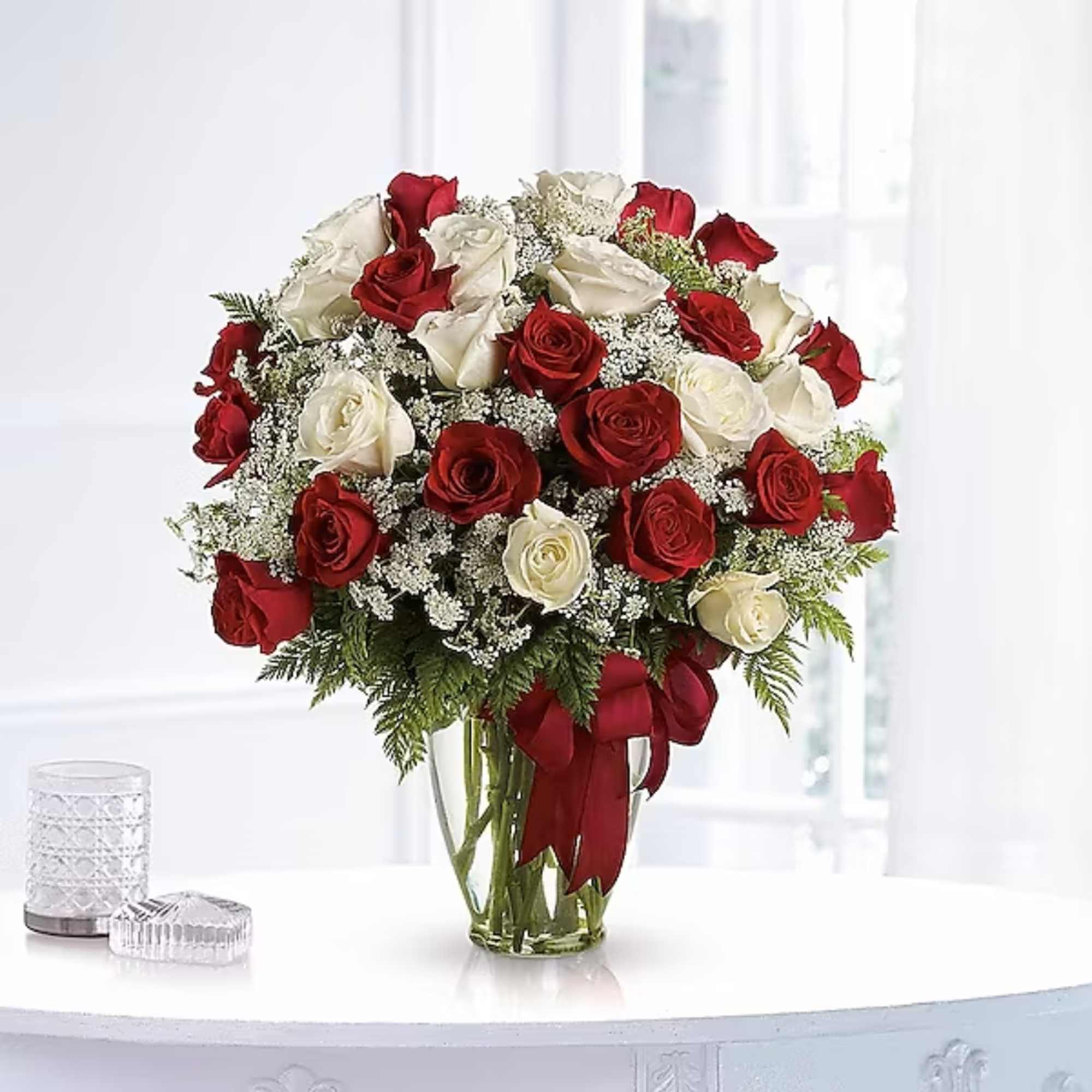 Red and white roses in a glass vase with a red ribbon