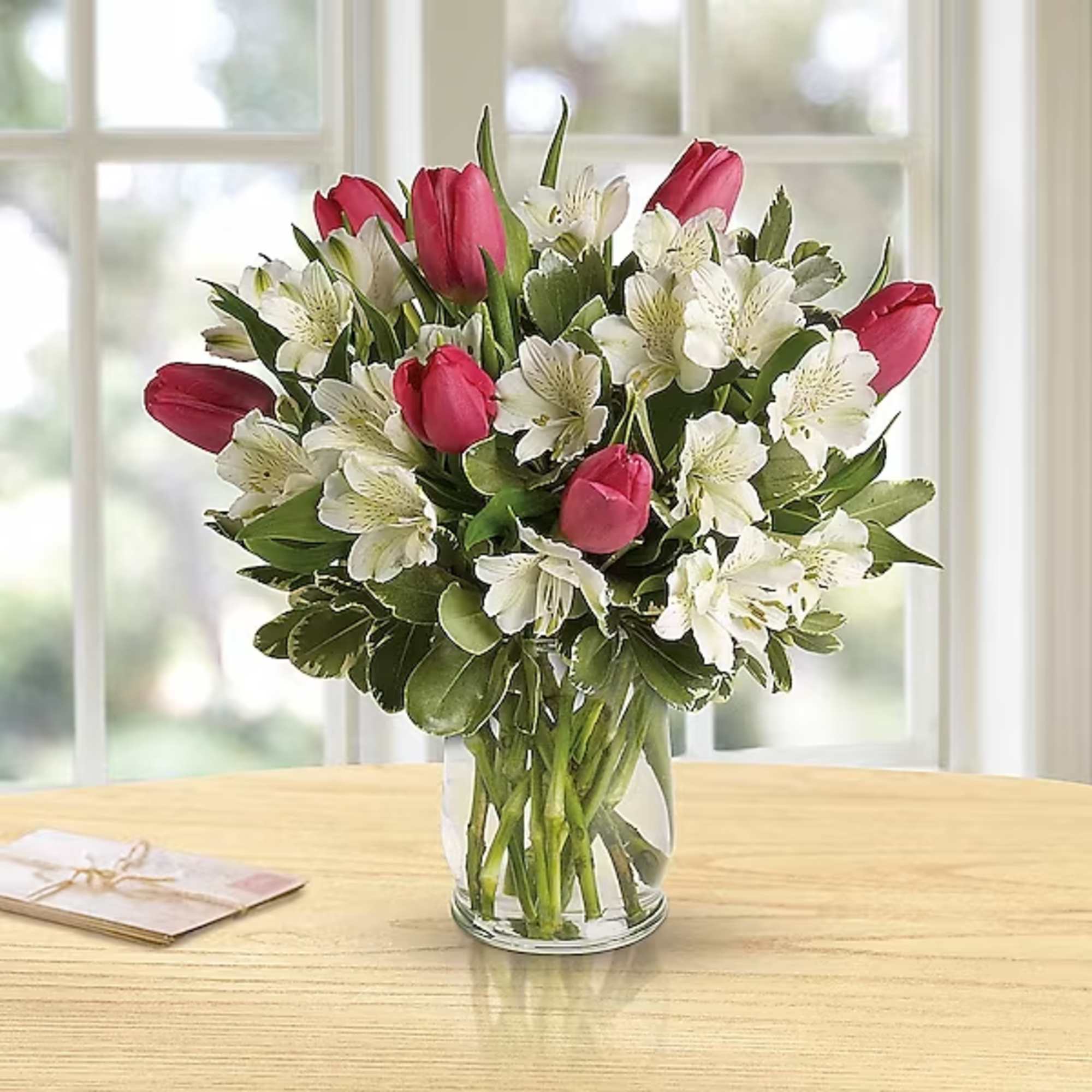 Pink tulips and white flowers in a clear glass vase