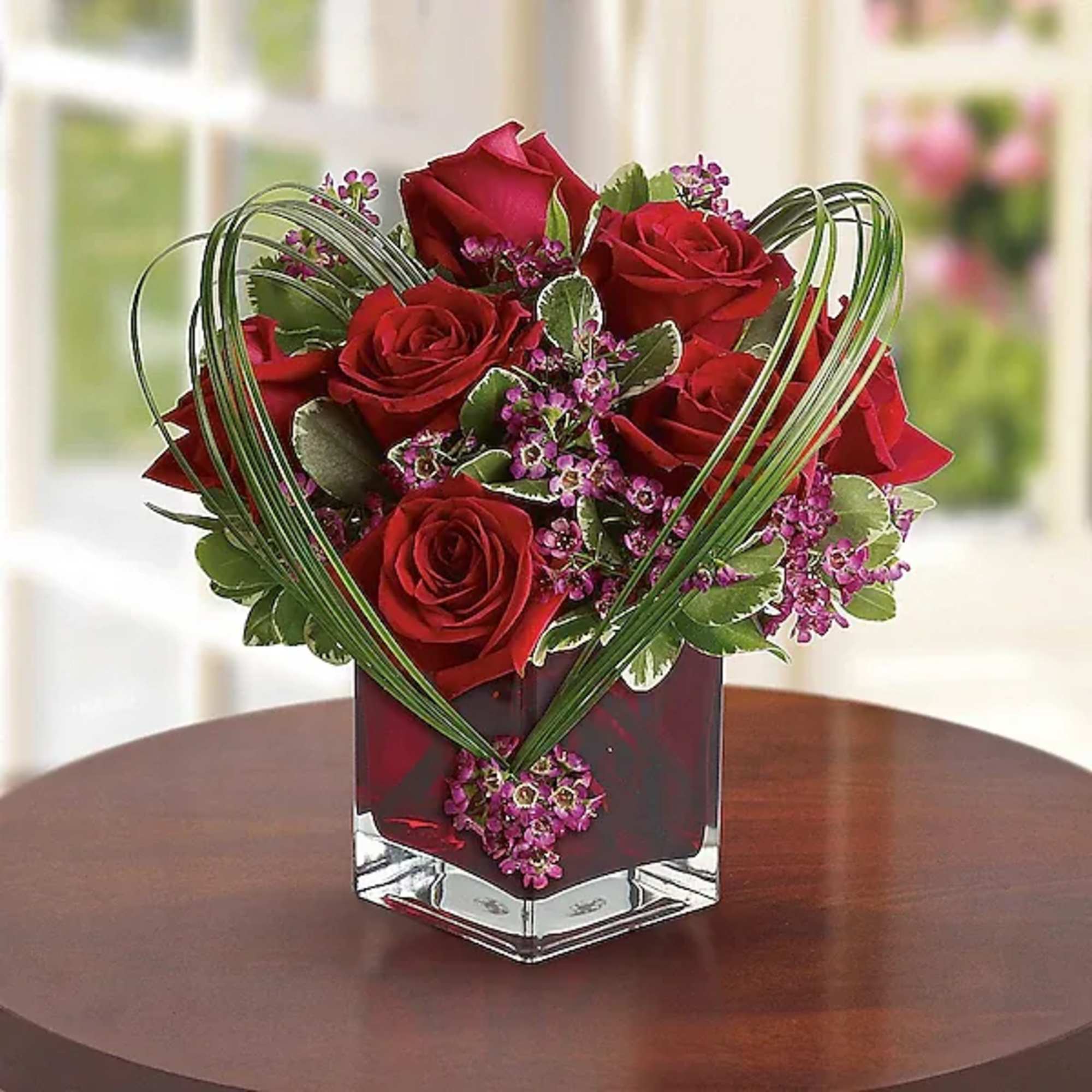 Red roses and purple filler flowers in a clear square vase