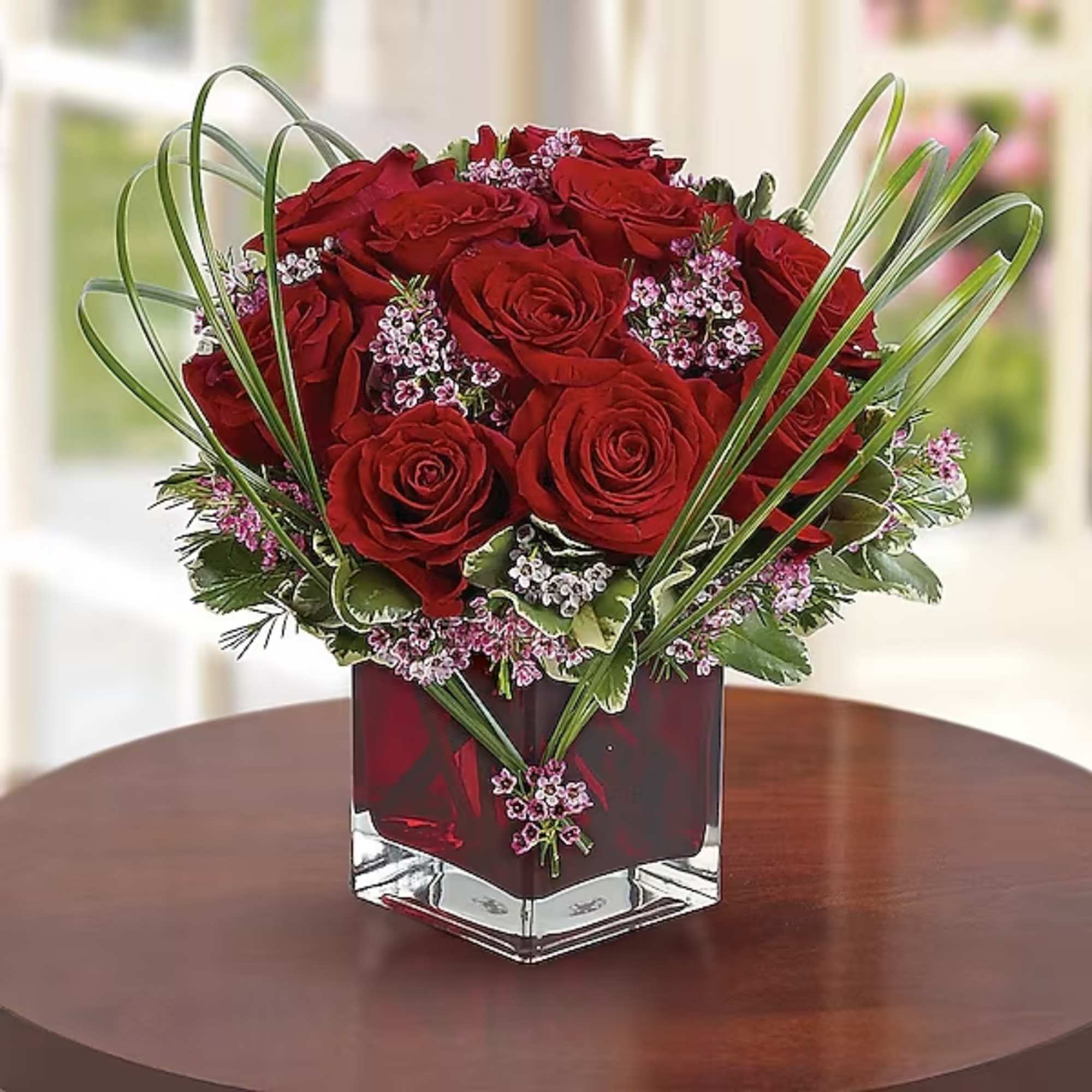 Red roses arranged in a square glass vase with small pink filler flowers