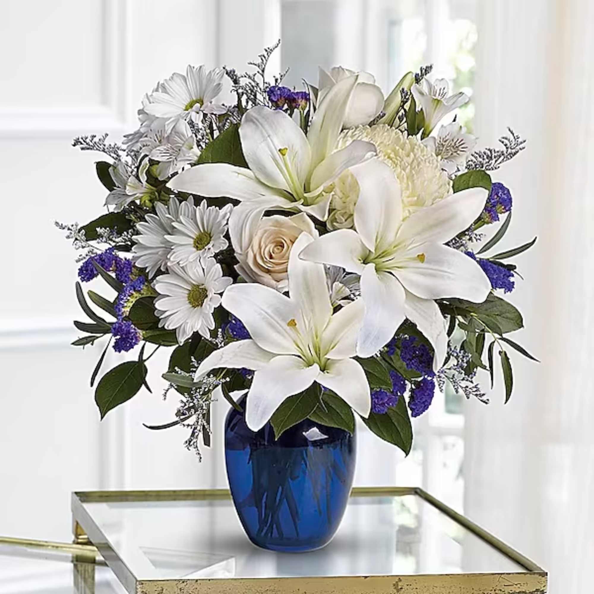 White lilies and daisies arranged in a blue glass vase
