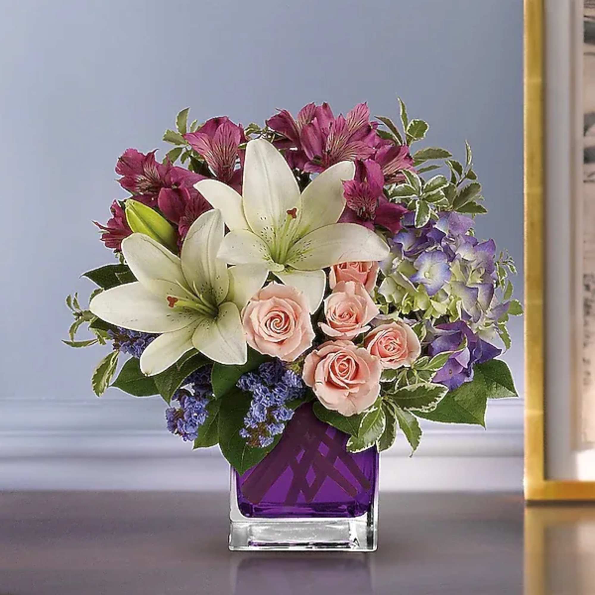 Bouquet of white lilies, pink roses, and purple flowers in a purple glass vase